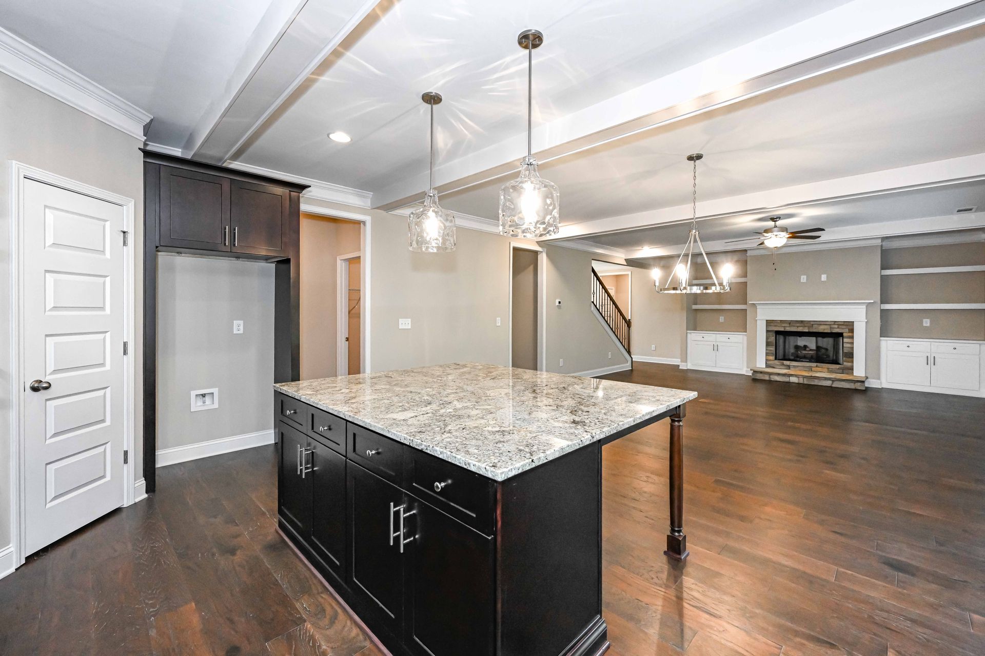Open-concept kitchen with granite island, dark wood floors, white cabinets, and fireplace in the living area