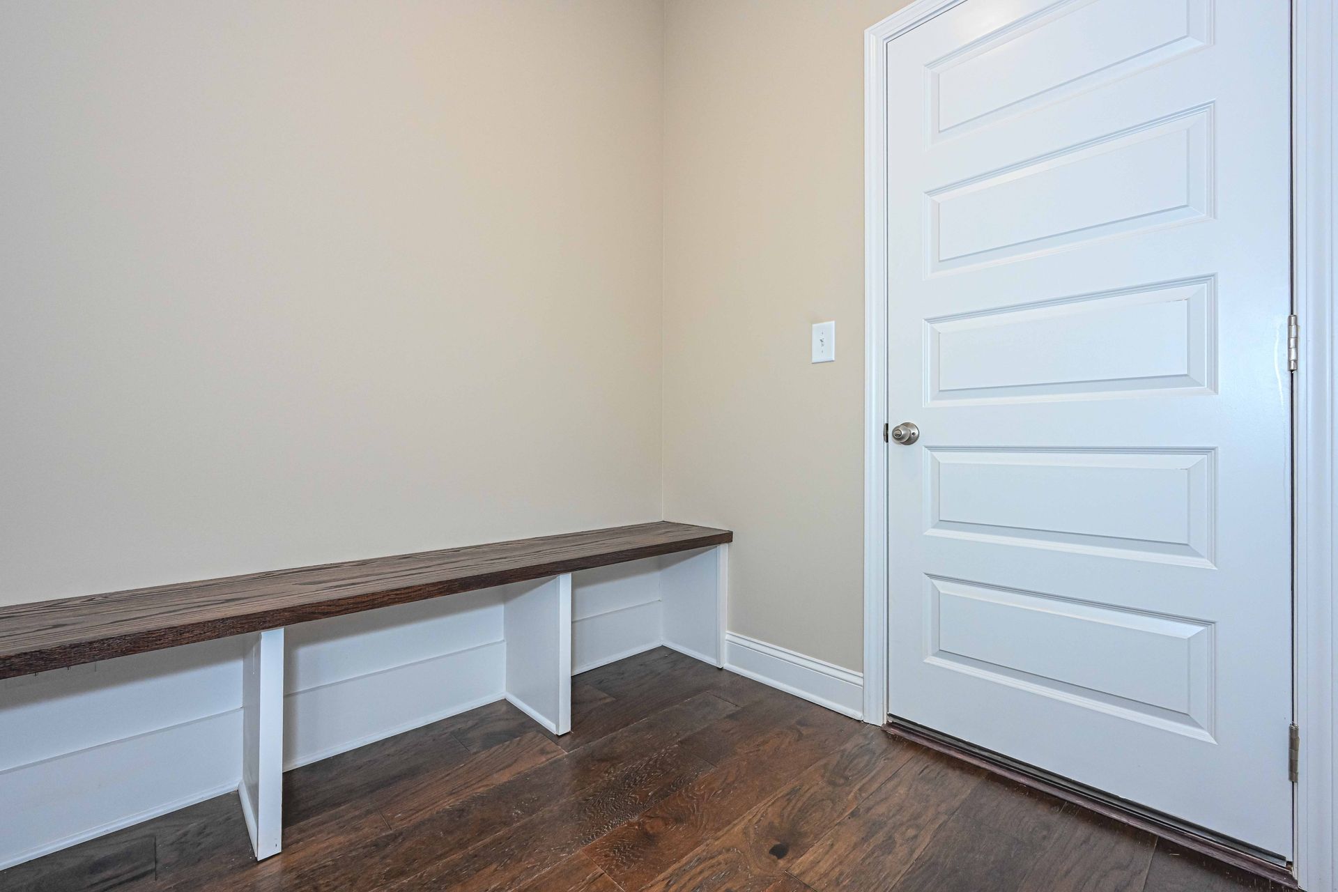 Empty room with white door, dark wood floor, and built-in bench with dark cushioned top.