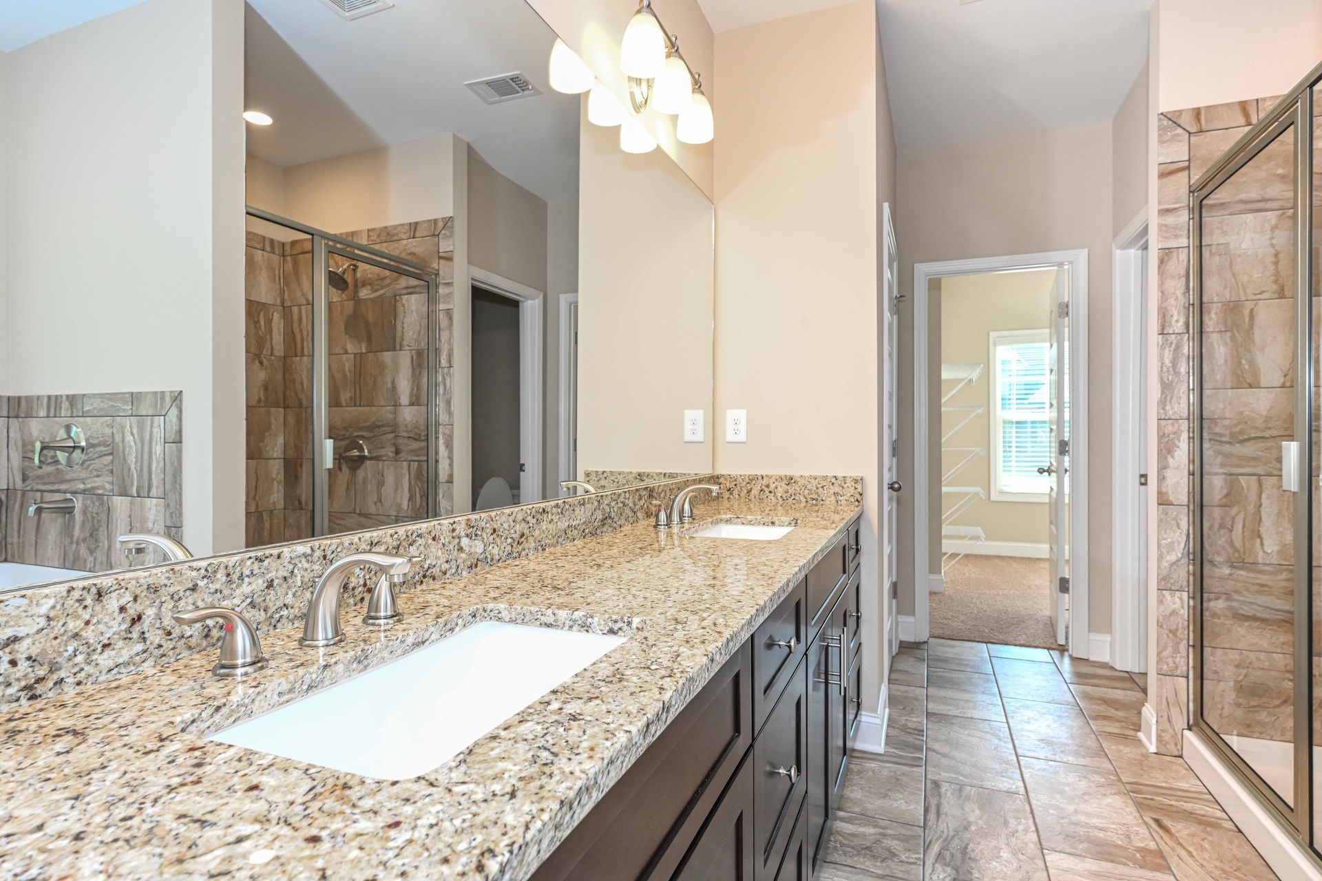Luxurious bathroom with granite double vanity, large mirrors, glass shower, and tiled floor