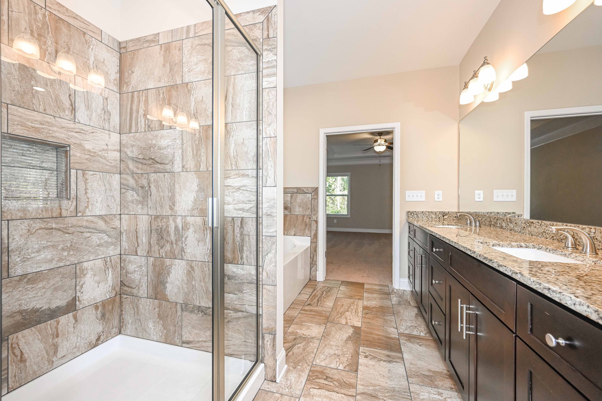 Modern bathroom with stone tile shower, glass door, and dark wood vanity with granite countertop