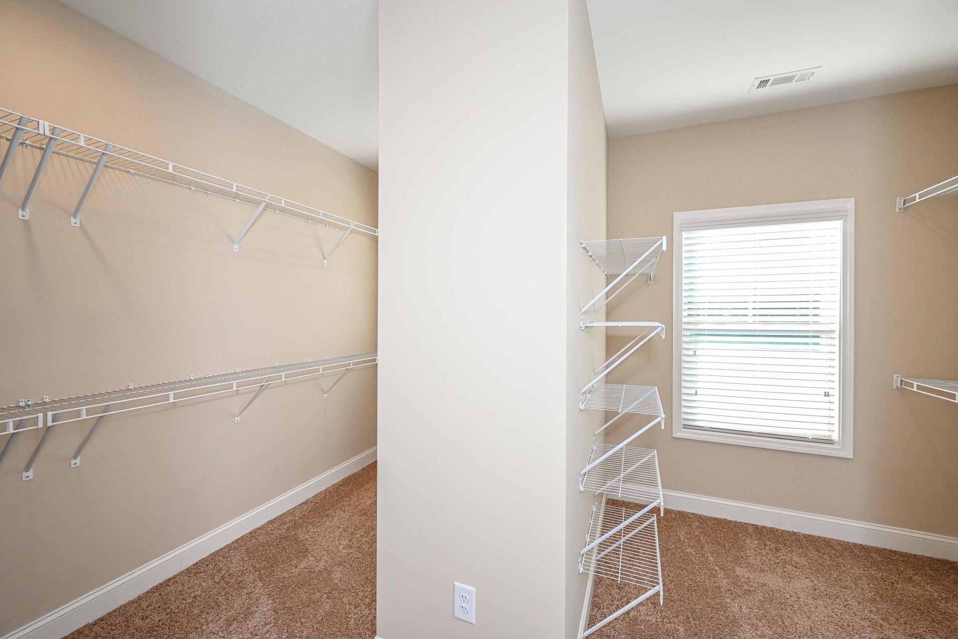 Empty walk-in closet with beige walls, white shelving, and brown carpet, viewed from the doorway