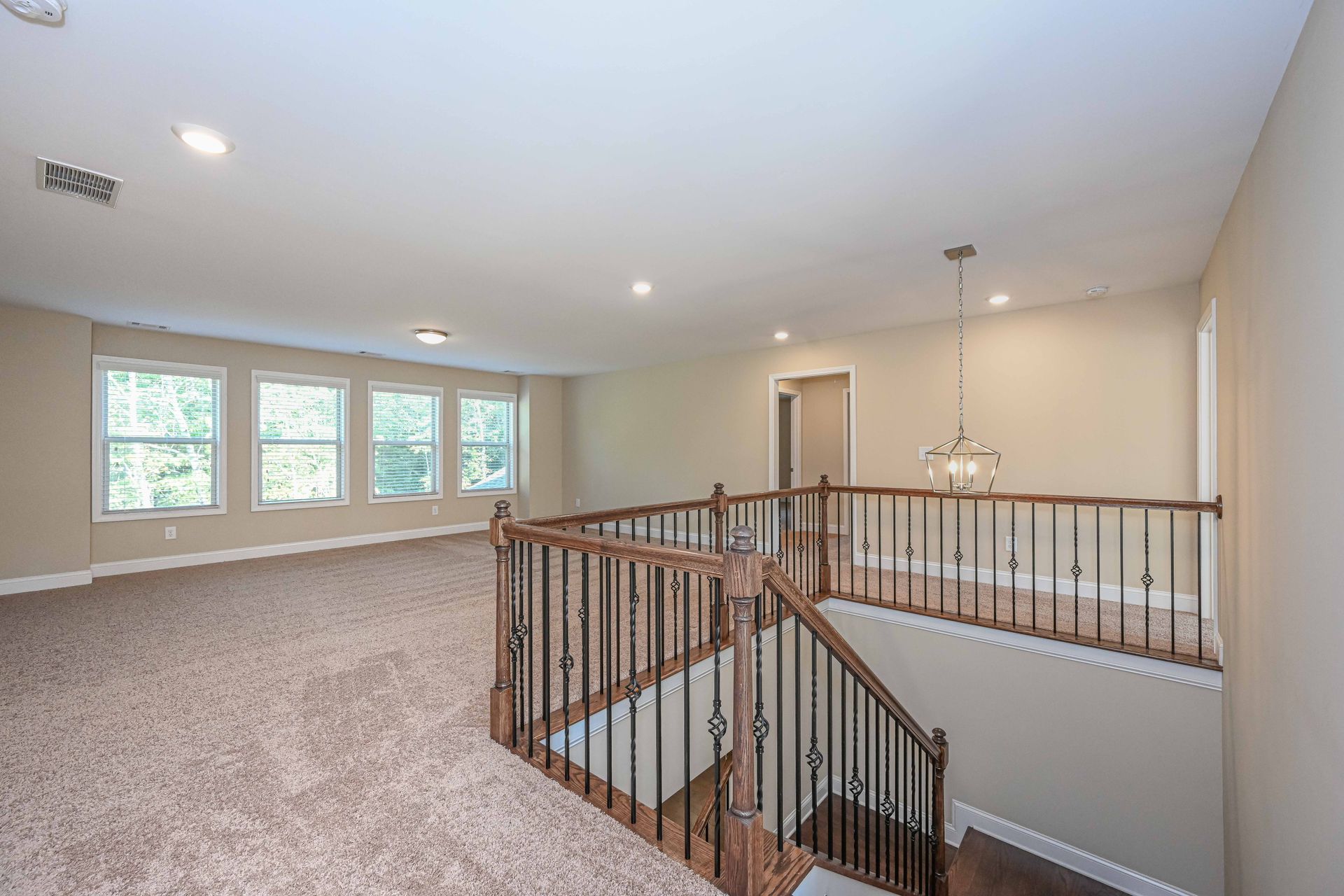 Spacious carpeted loft landing with railing, staircase, chandelier, and large windows letting in daylight
