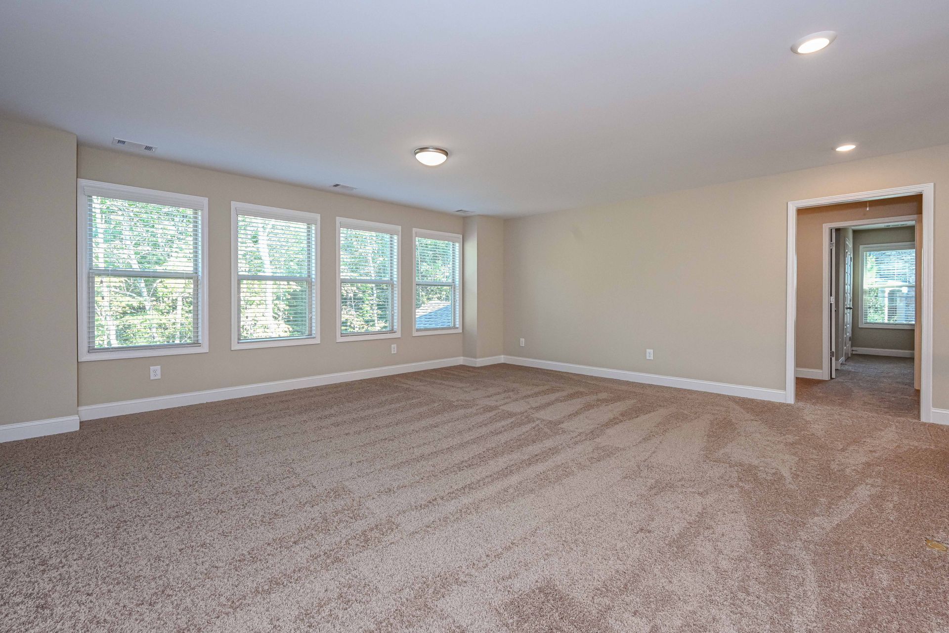 Empty beige living room with carpet, recessed lights, large windows, and an open doorway