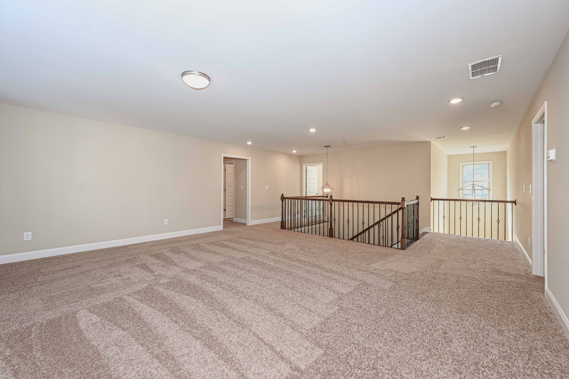 Empty beige carpeted loft with recessed lighting, railing, and adjacent hallway doorways
