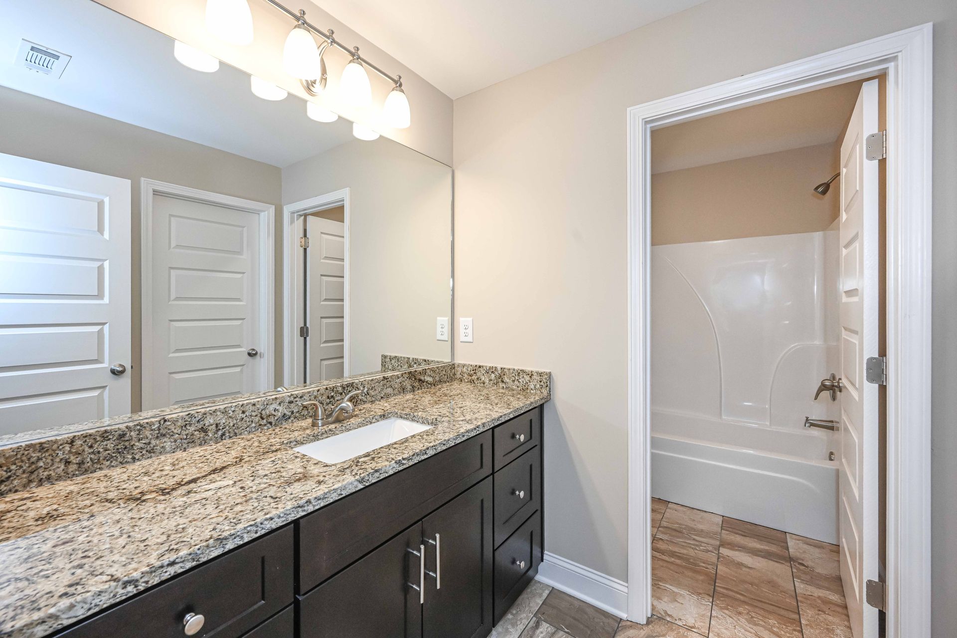 Bathroom vanity with granite countertop, large mirror, and open doorway to a tub shower.