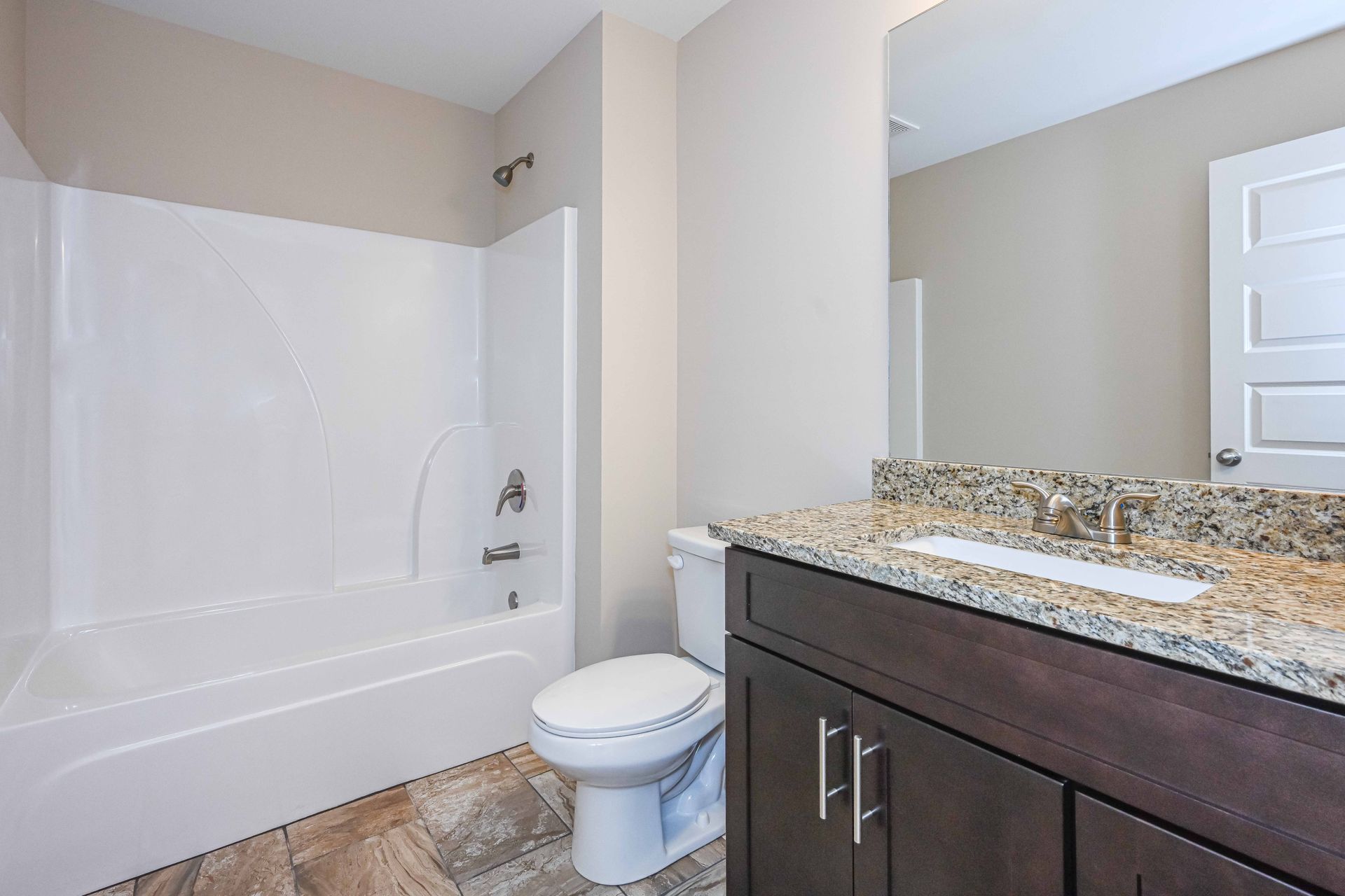 Bathroom with white tub, toilet, and dark vanity with granite countertop and mirror.