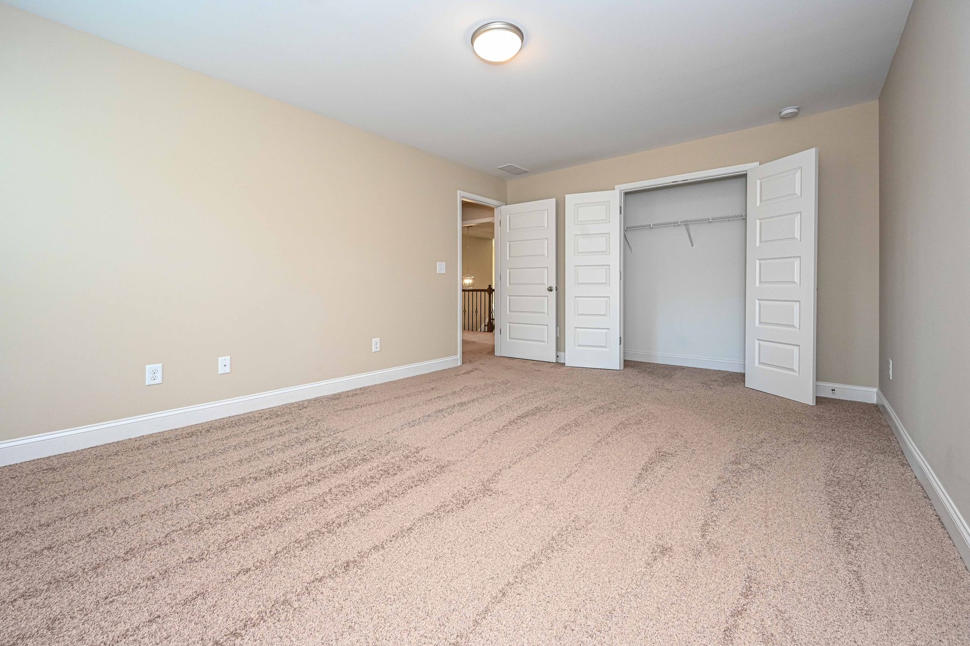 Empty beige bedroom with carpet, closet doors open, and a ceiling light.