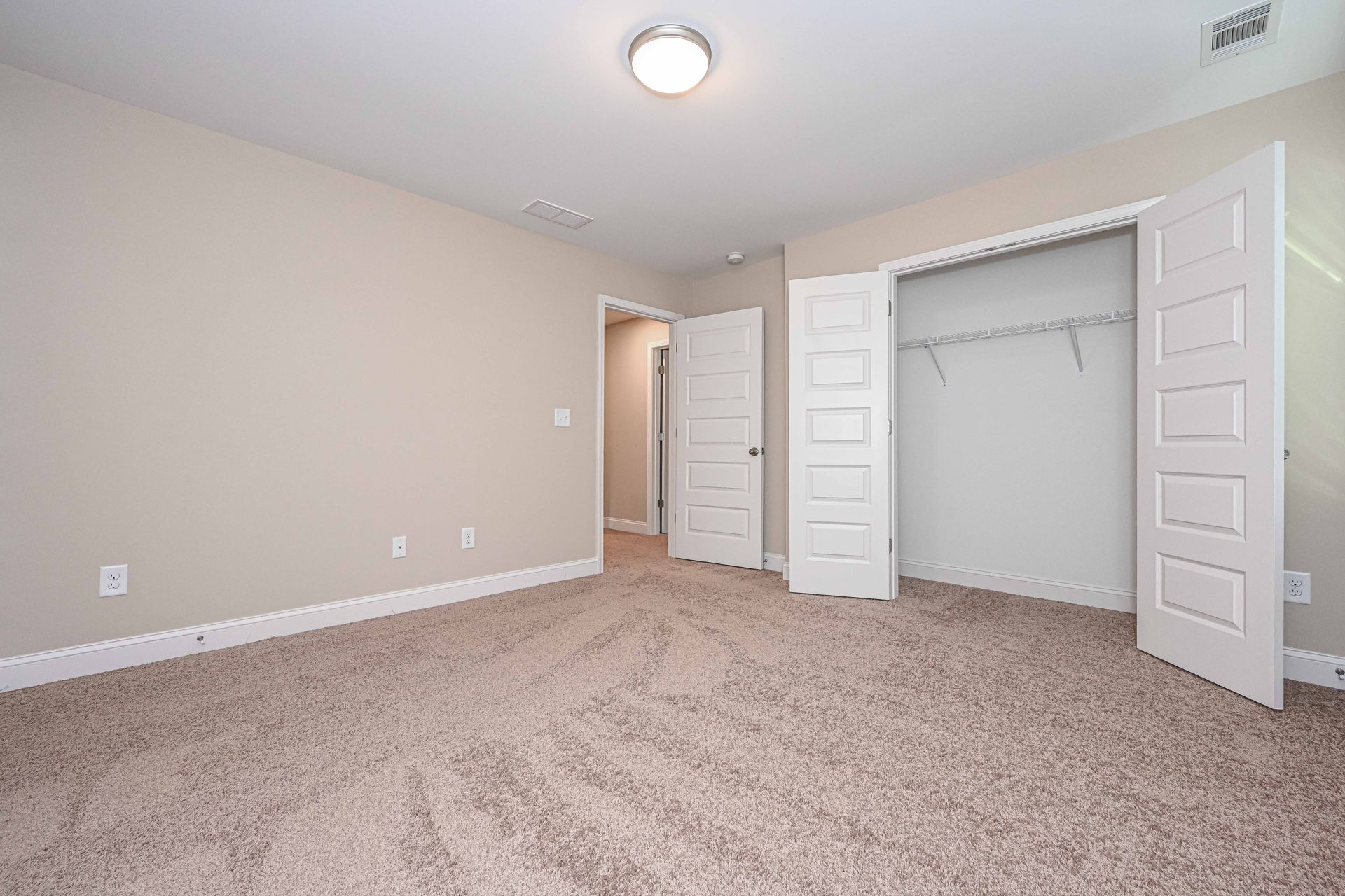 Empty beige bedroom with carpet, open closet doors, and a ceiling light