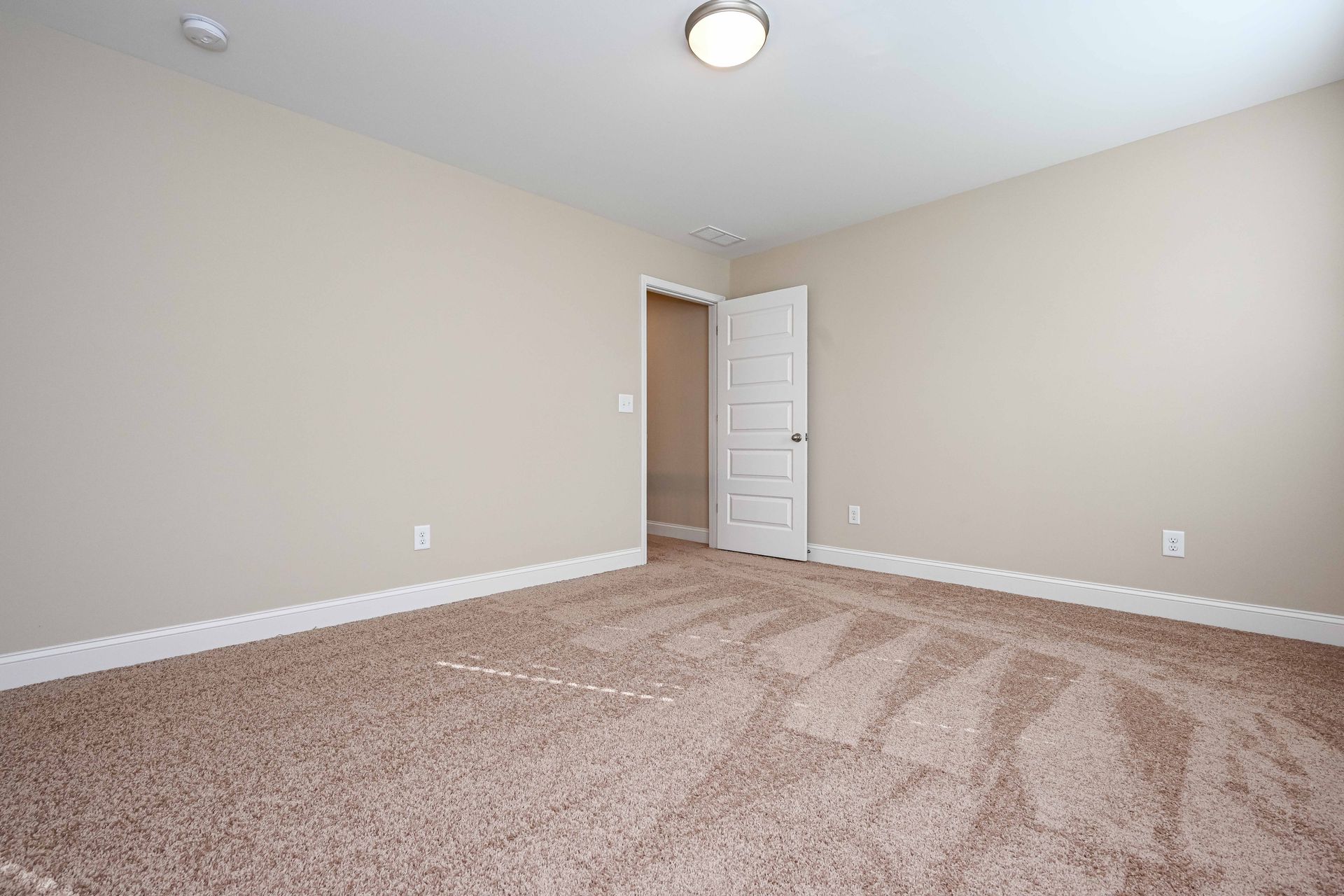 Empty beige carpeted bedroom with white door and ceiling light