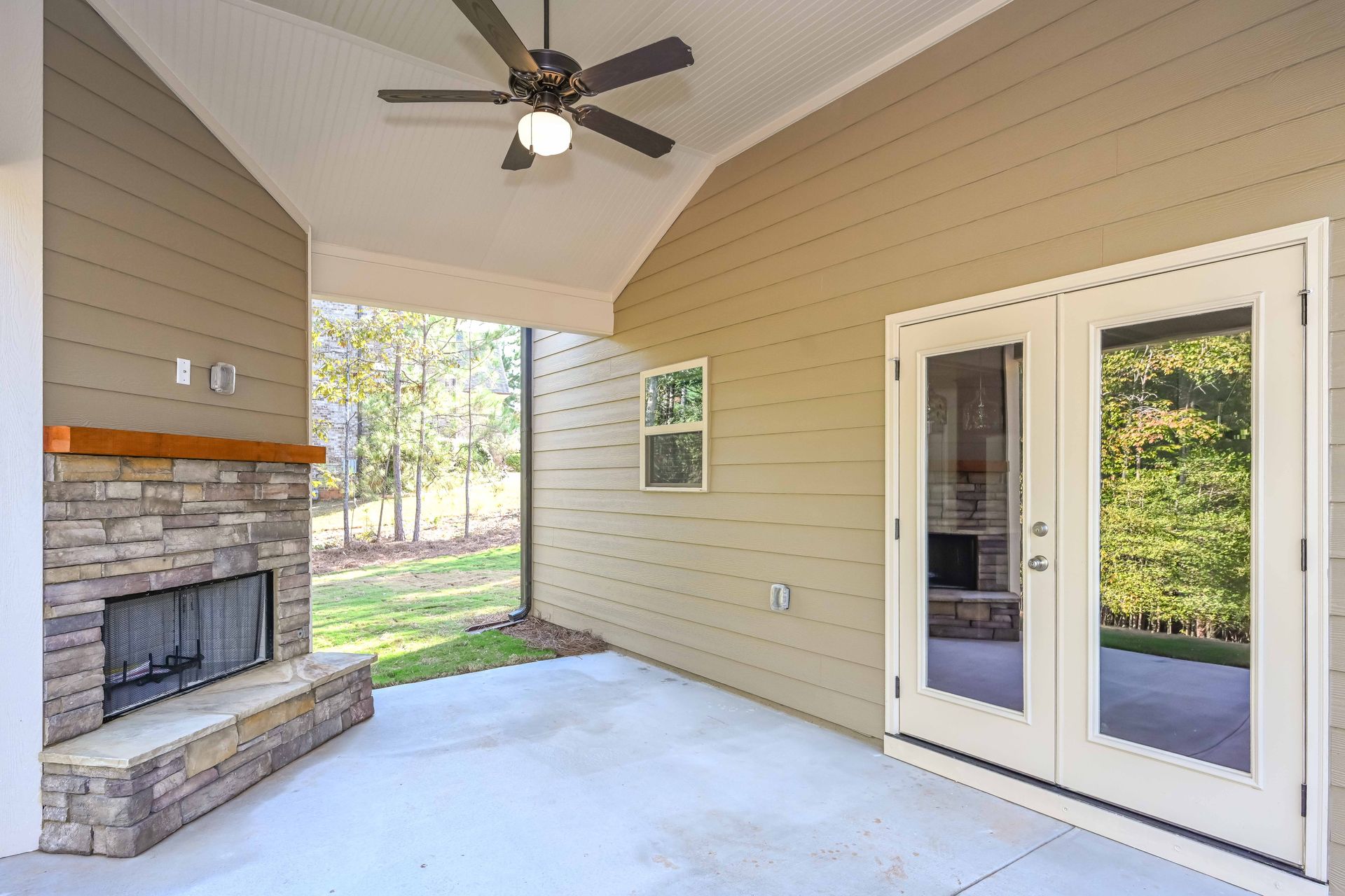Covered patio with fireplace, ceiling fan, and white French doors overlooking a backyard.