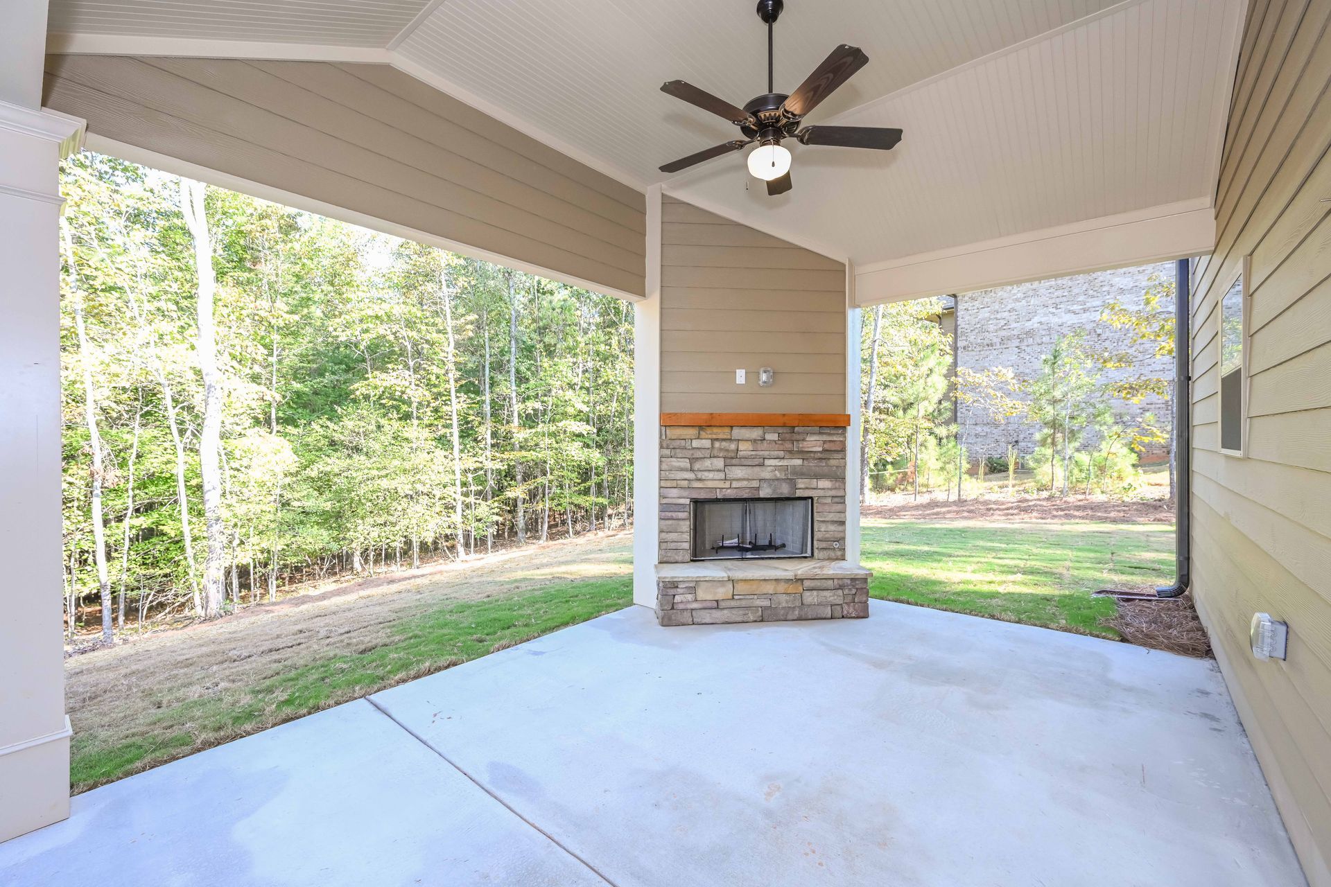 Covered patio with ceiling fan, fireplace, and wooded backyard view