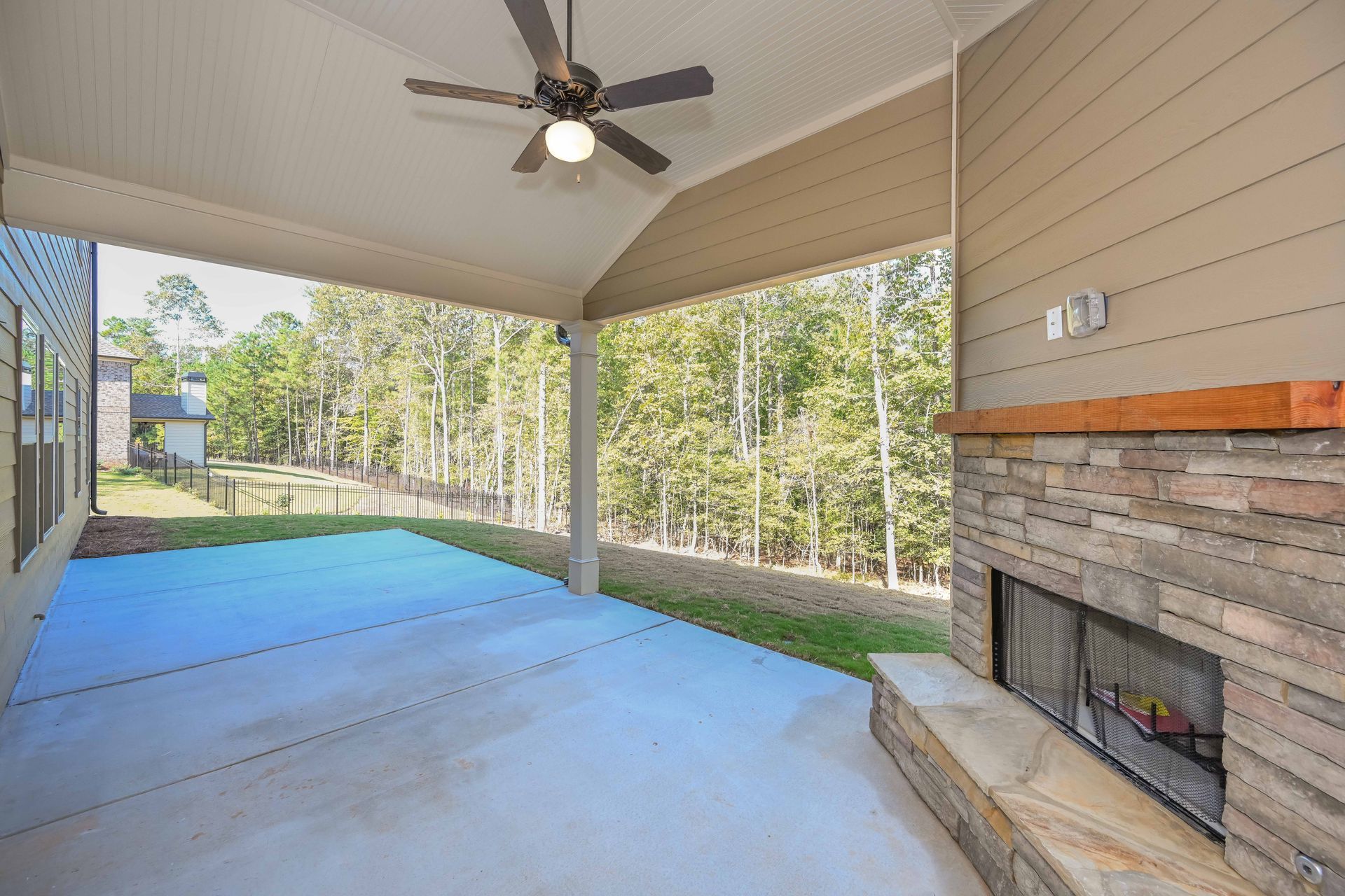 Covered patio with ceiling fan, fireplace, and open view of trees beyond the railing