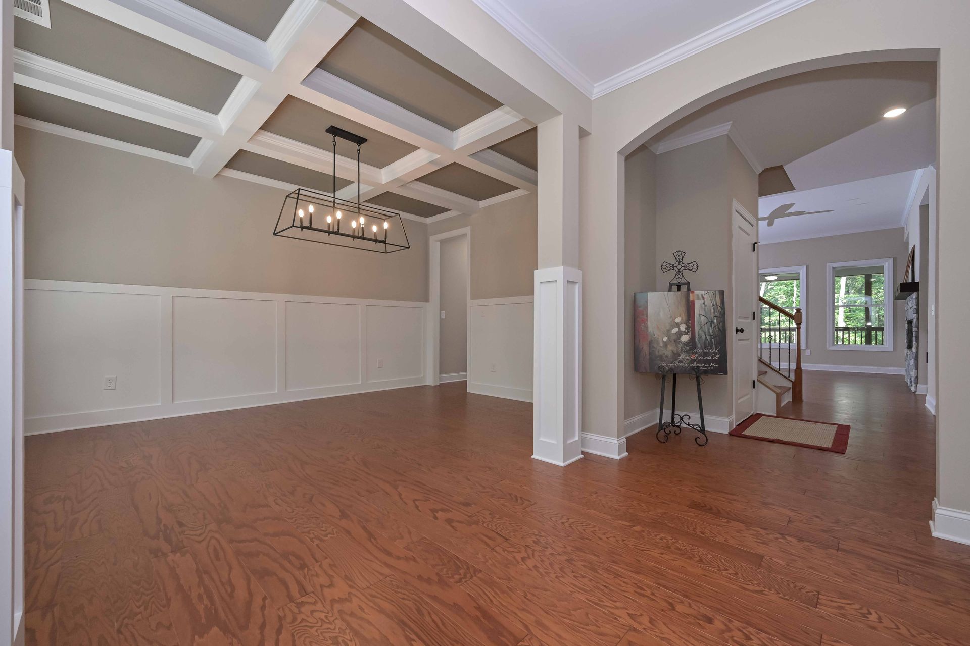 Spacious empty dining room with hardwood floors, tray ceiling, chandelier, and arched entryway to a bright foyer
