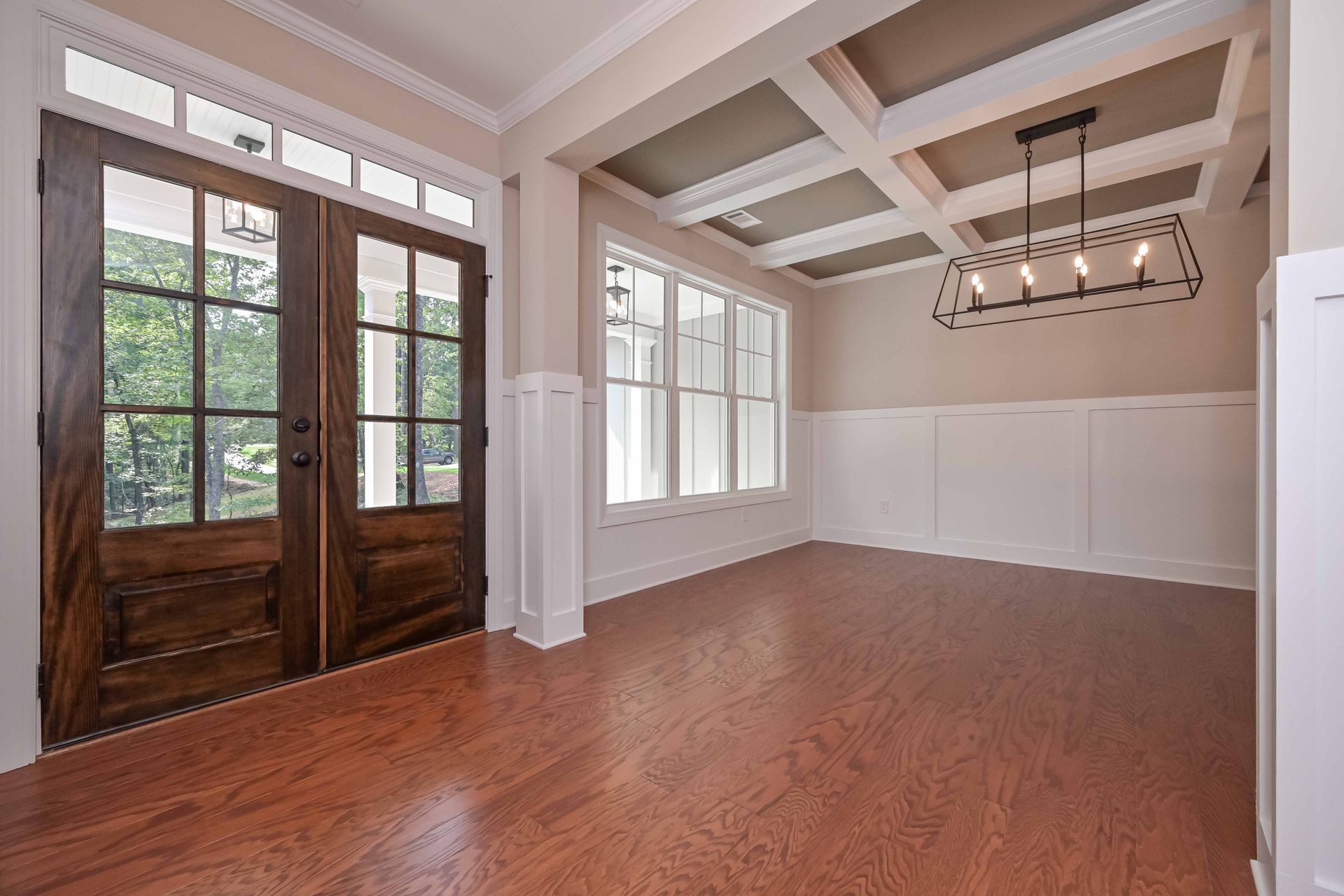 Empty dining room with hardwood floors, white wainscoting, beamed ceiling, and wood-framed glass doors