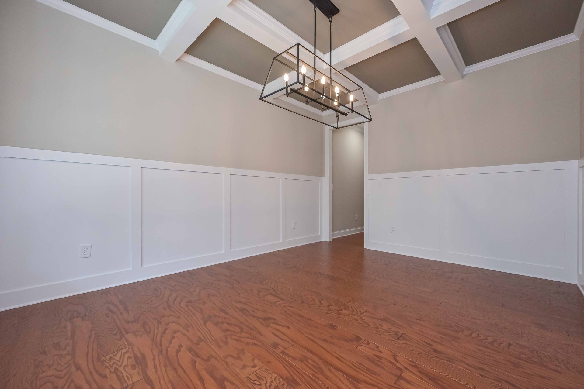 Empty dining room with wood floor, white wainscoting, vaulted ceiling, and a hanging chandelier