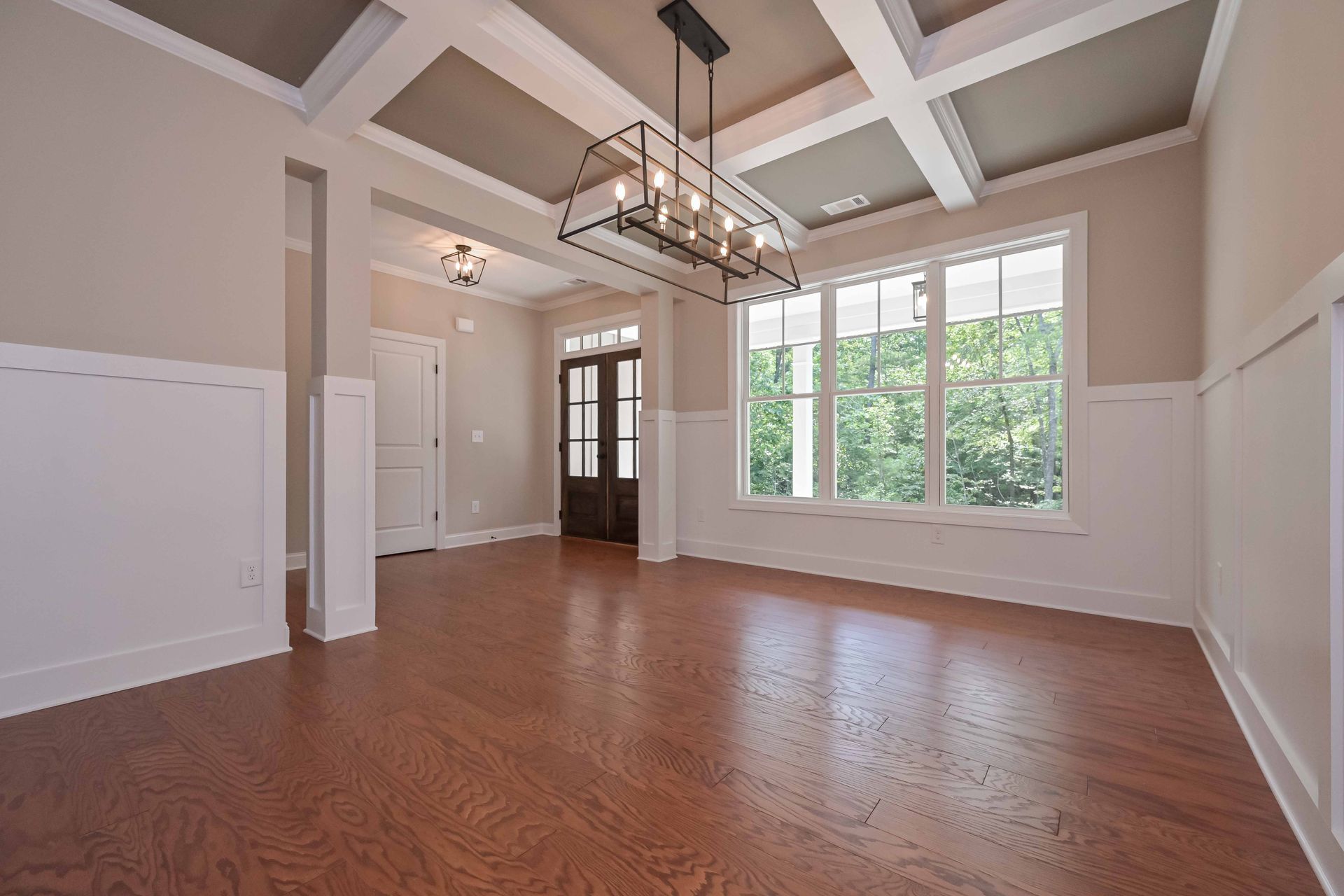 Empty dining room with hardwood floors, coffered ceiling, chandelier, and large windows overlooking trees