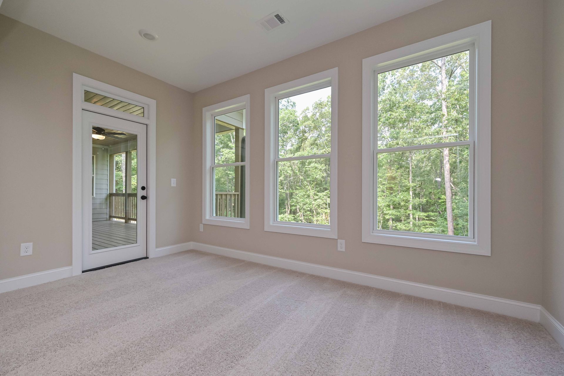 Empty beige bedroom with carpet, tall windows, and a mirrored closet door
