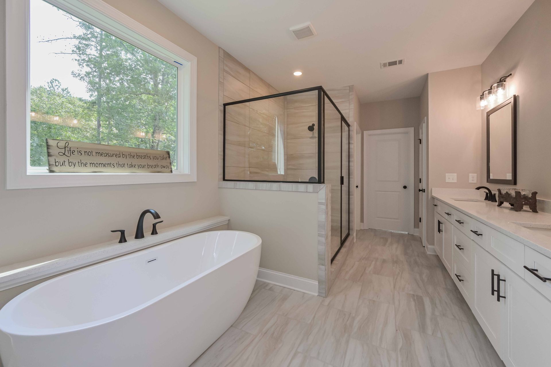 Bright modern bathroom with freestanding tub, glass shower, double vanity, and large window