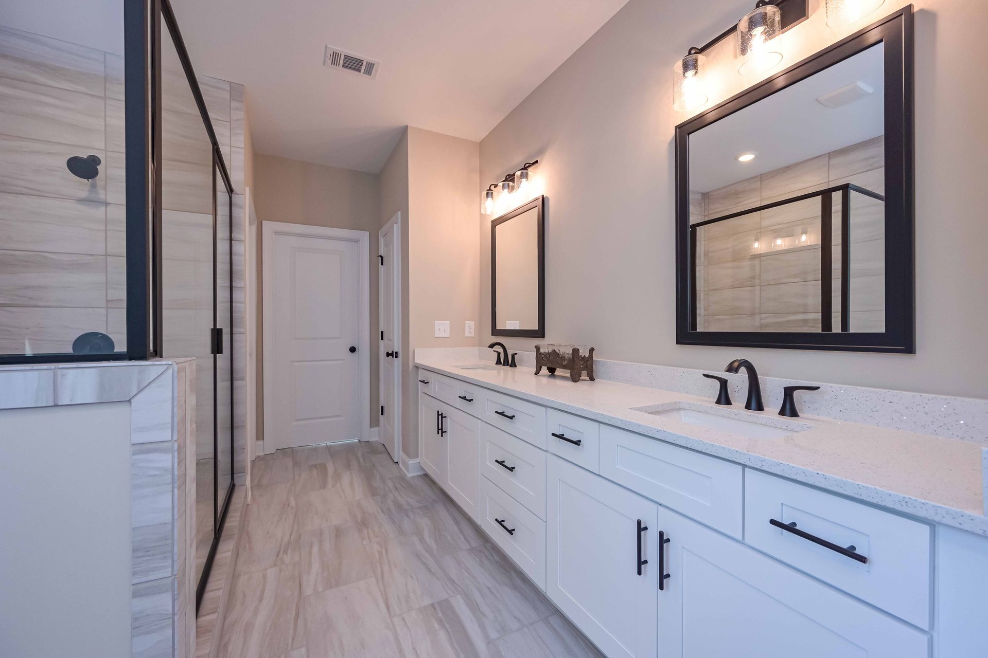 Modern bathroom with double vanity, large mirrors, black fixtures, and white cabinetry