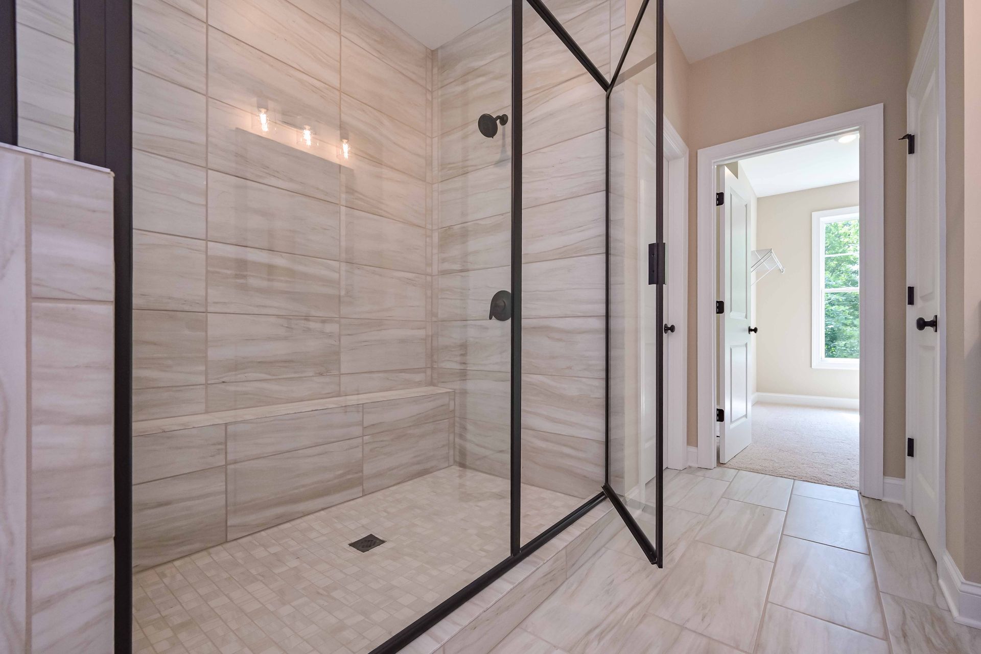 Modern bathroom with a large walk-in shower, black-framed glass door, and light tile flooring.