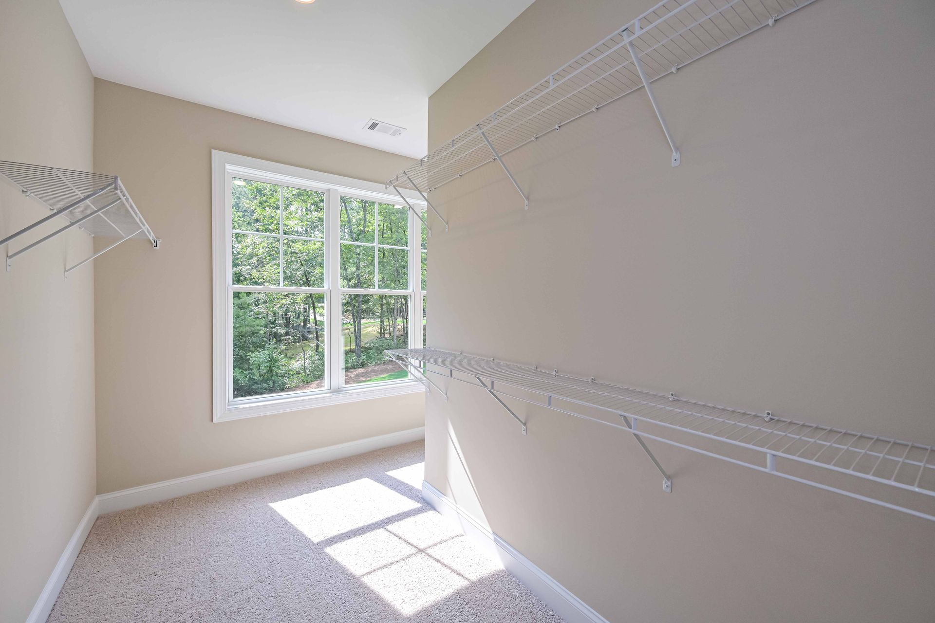 Empty beige walk-in closet with wire shelves and a window letting in sunlight.