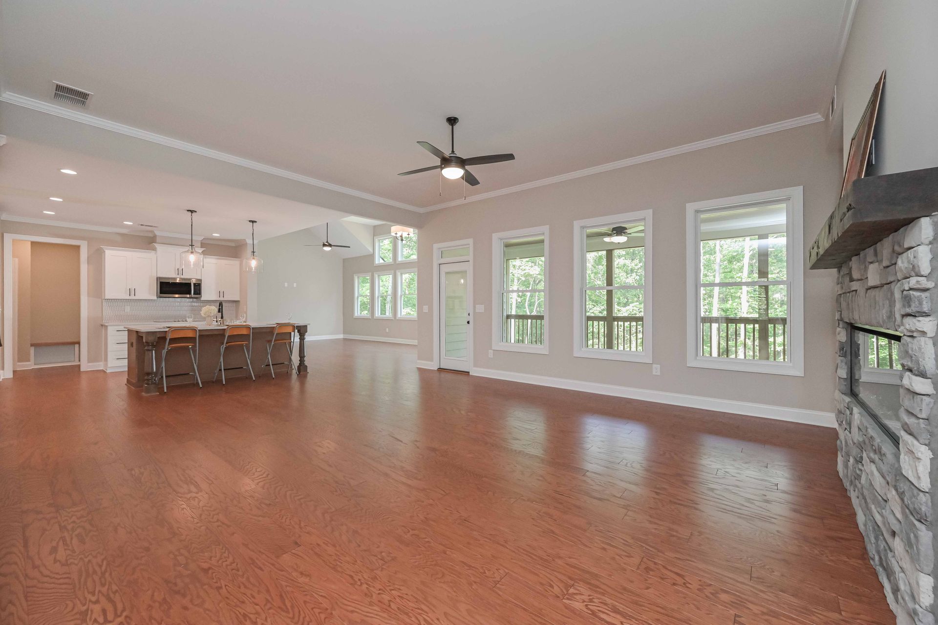 Spacious open-concept living room with hardwood floors, stone fireplace, ceiling fan, and kitchen island beyond.