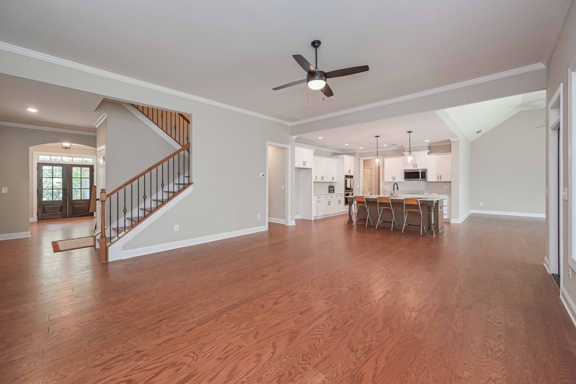 Spacious open-concept living room with hardwood floors, staircase, ceiling fan, and white kitchen island