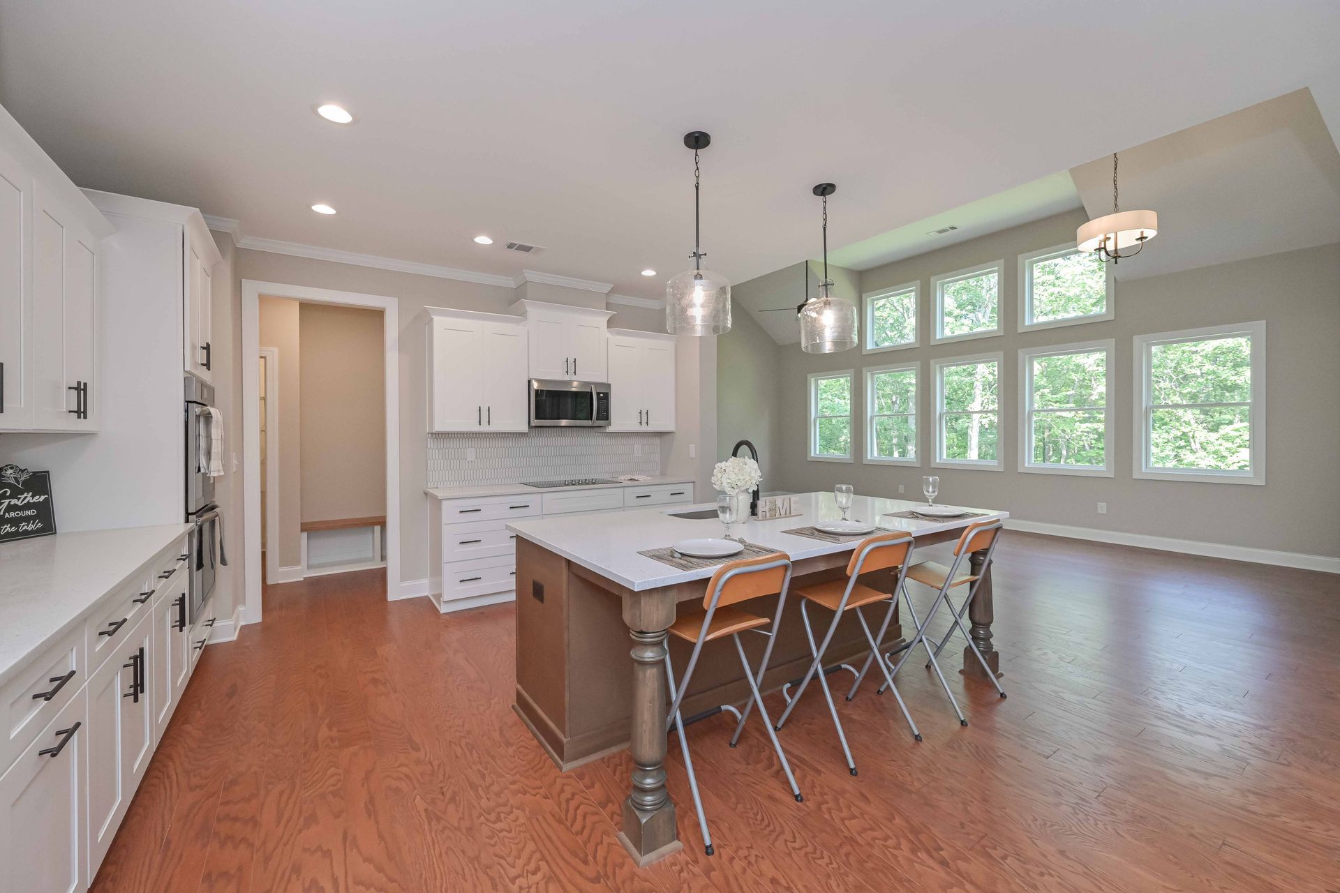 Bright modern kitchen with island, bar stools, white cabinets, and large windows over hardwood floors