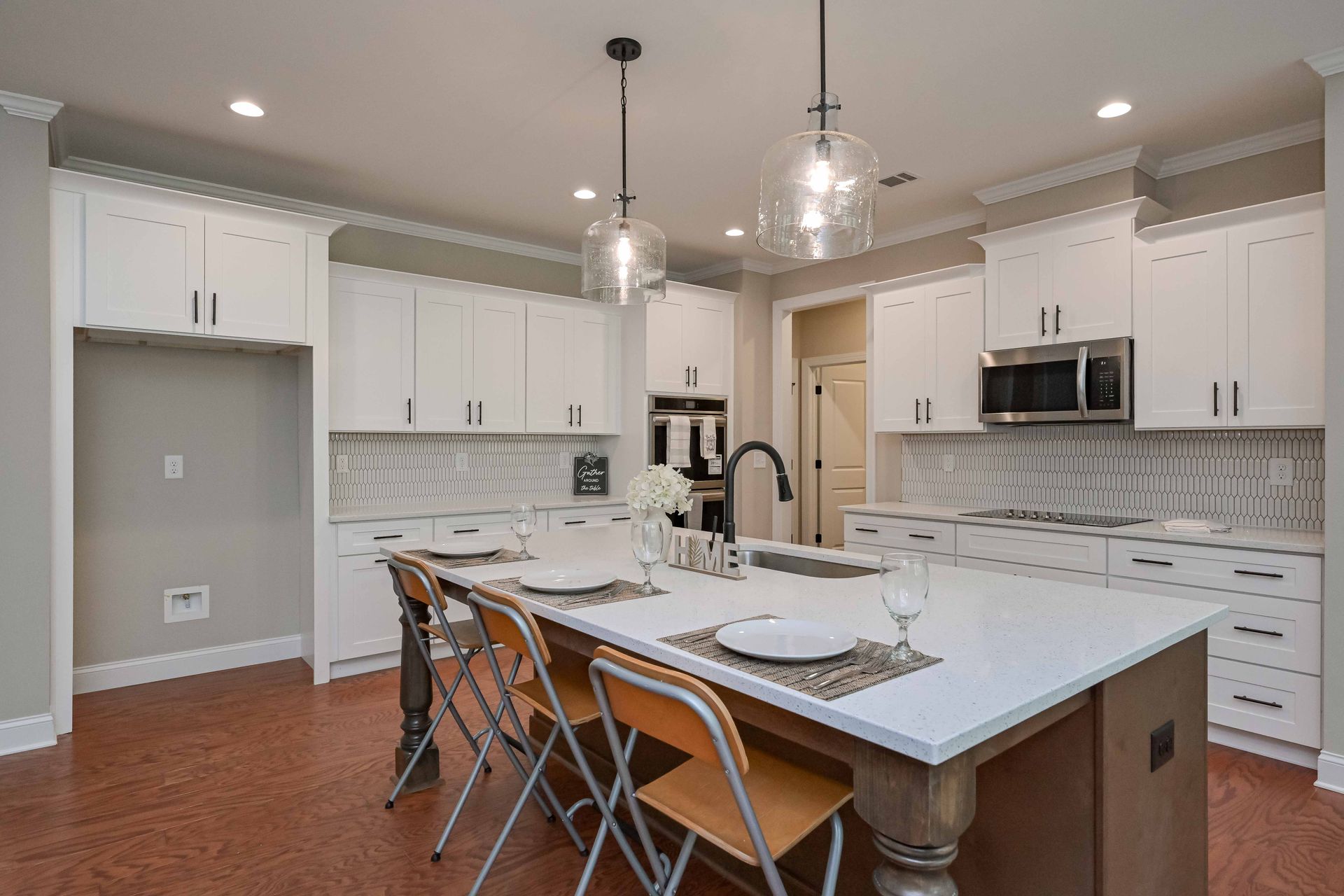 Modern kitchen with white cabinets, island, pendant lights, and a dining table set for a meal.