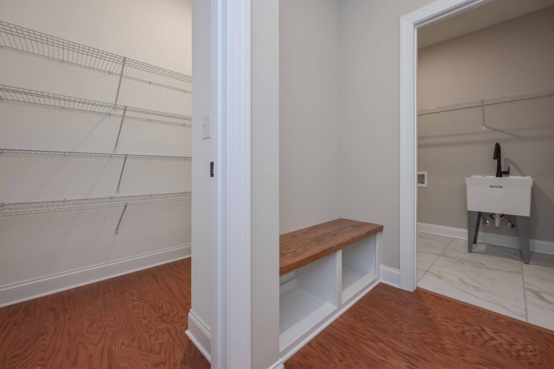 Walk-in closet with white shelves, wood flooring, and a vanity sink in an adjoining bathroom