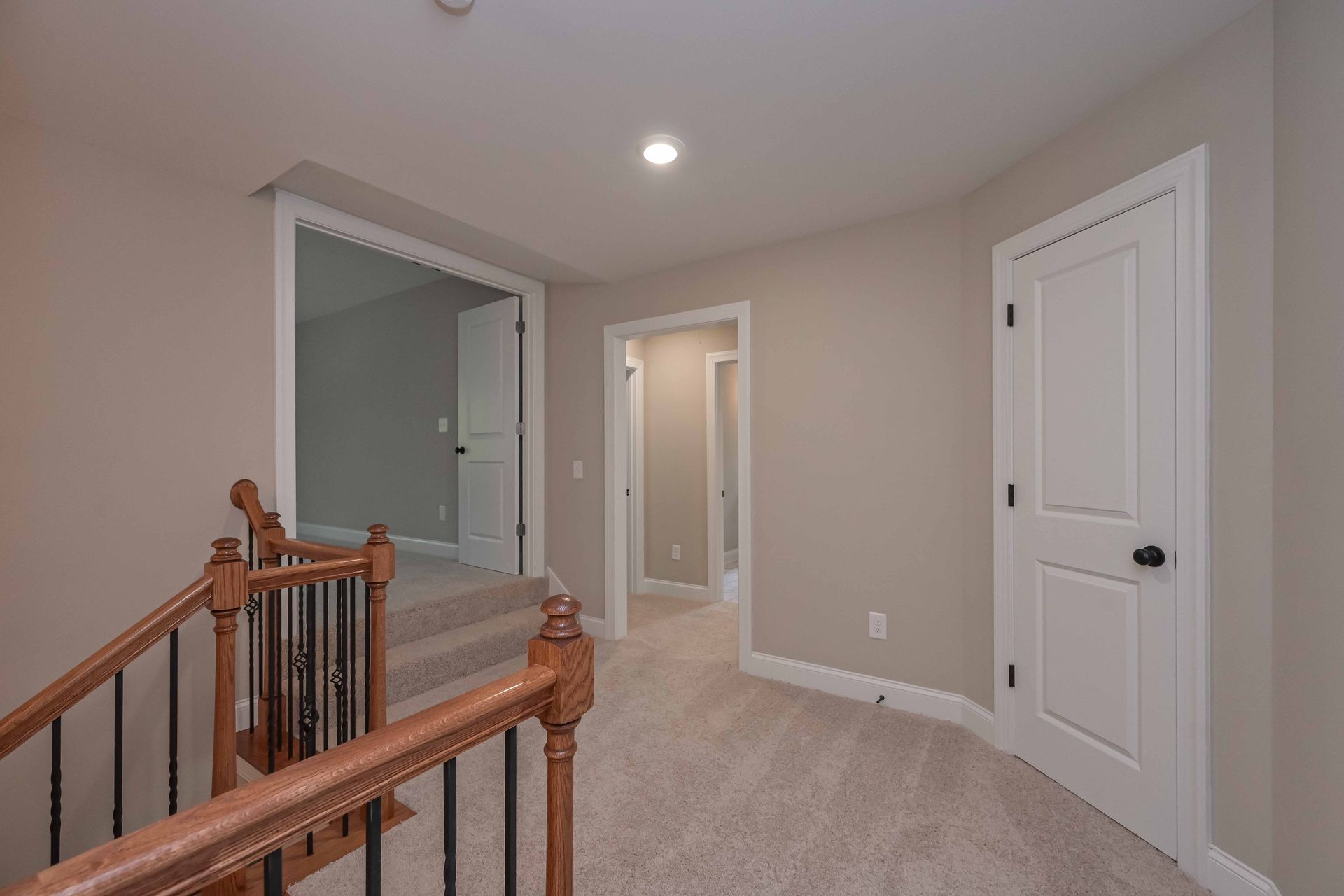 Carpeted upstairs hallway with white doors, beige walls, and a wooden railing by the stairs.