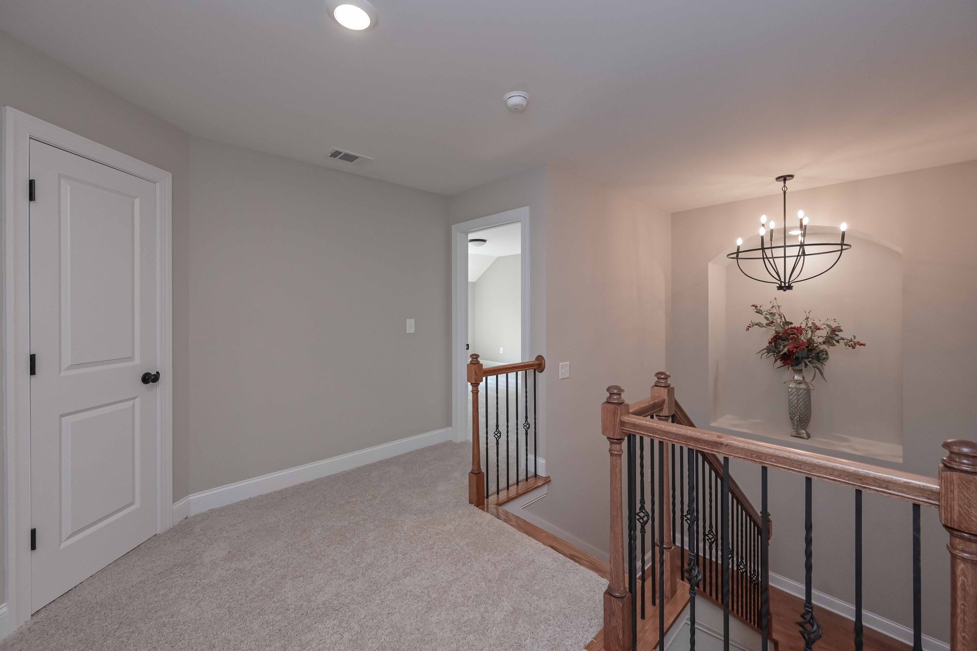 Carpeted upstairs landing with gray walls, white doors, wooden railing, and a chandelier in the hall.