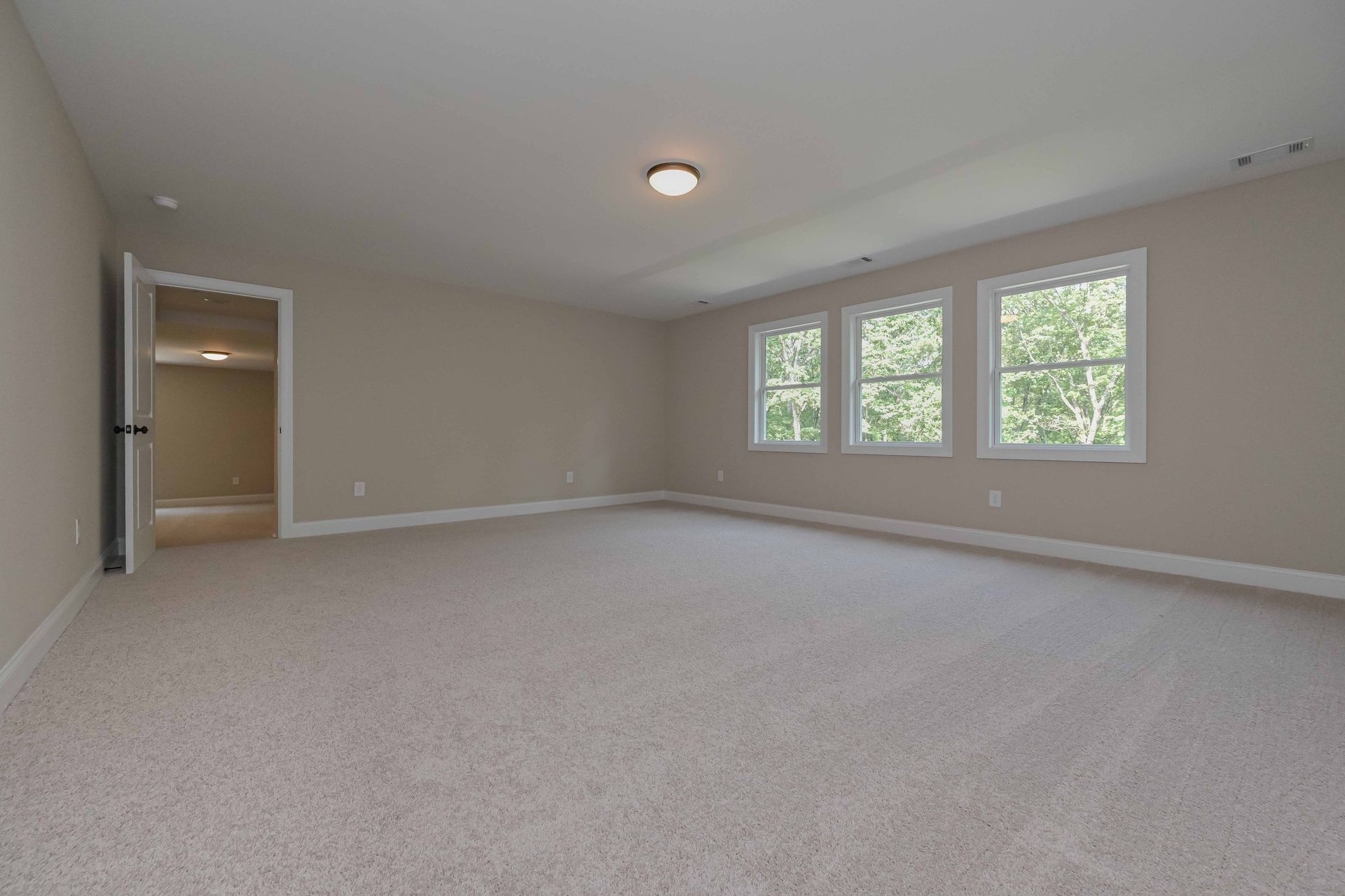 Empty beige carpeted room with recessed light, closet, and three windows letting in natural light
