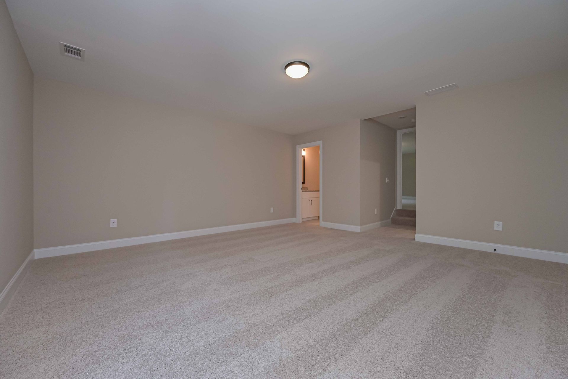 Empty beige carpeted living room with recessed light and hallway openings