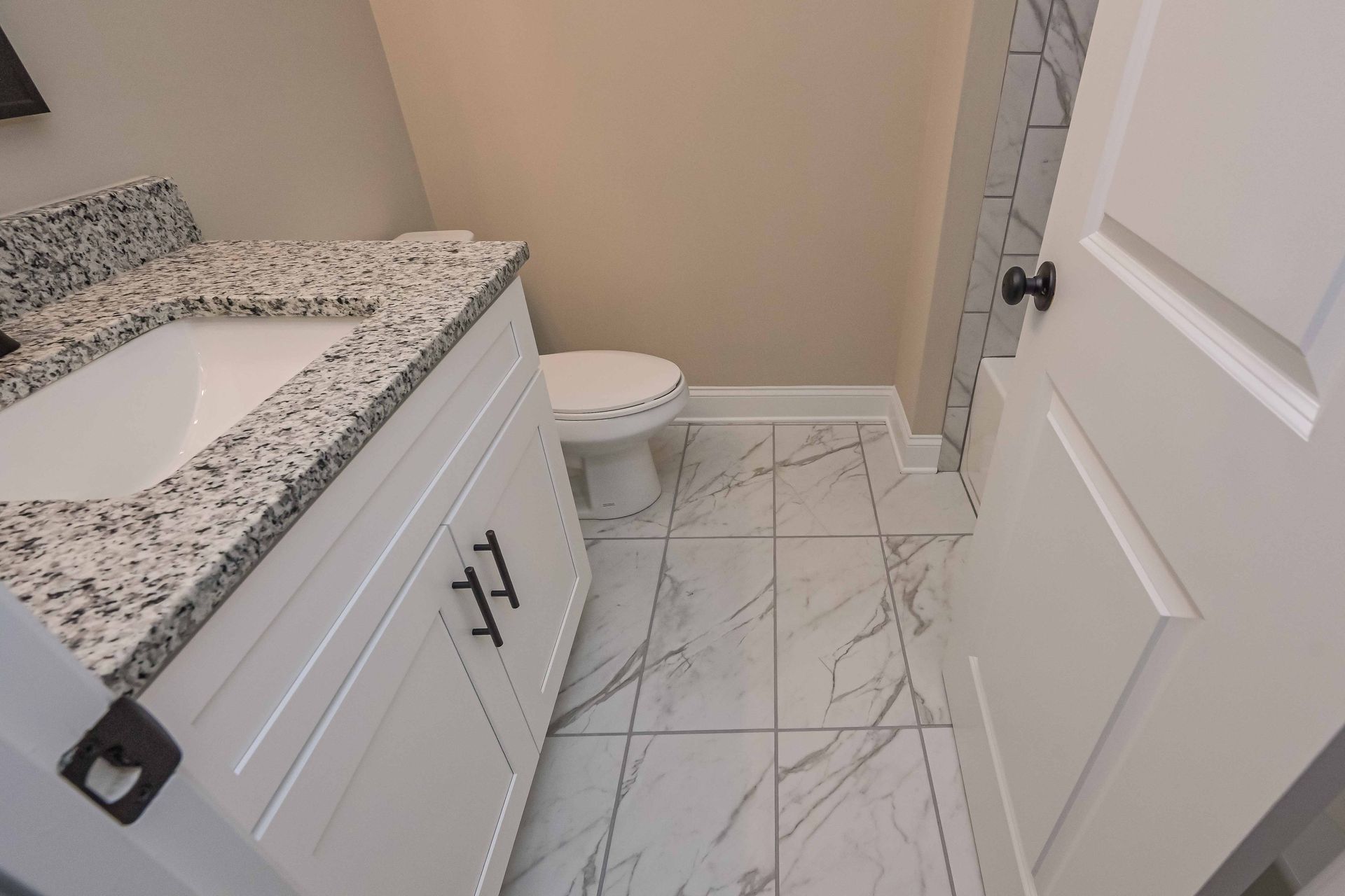Small bathroom with white vanity, speckled countertop, toilet, and marble-look tile floor.