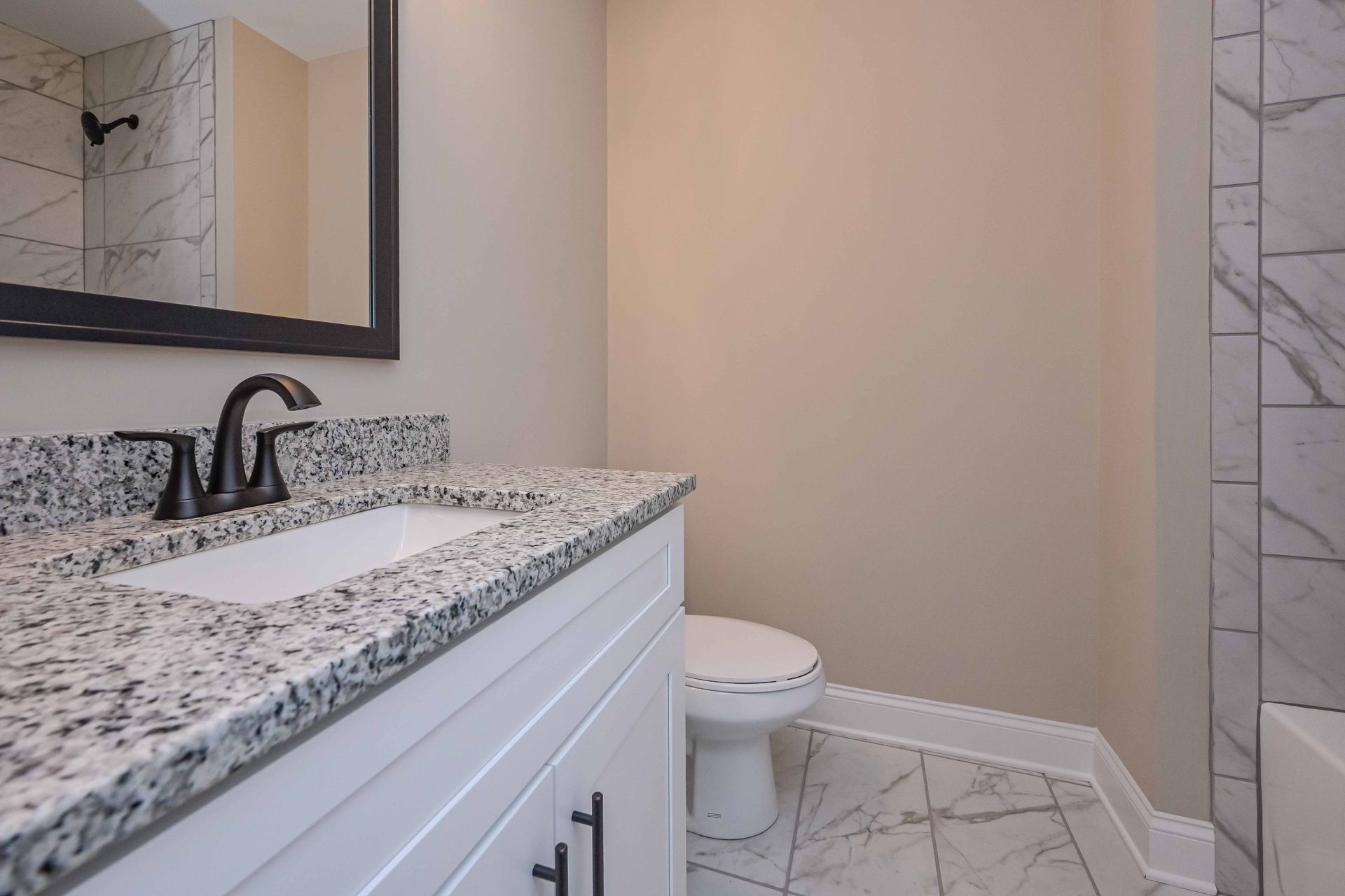 Small bathroom with granite vanity, black faucet, white toilet, and marble tile floor.