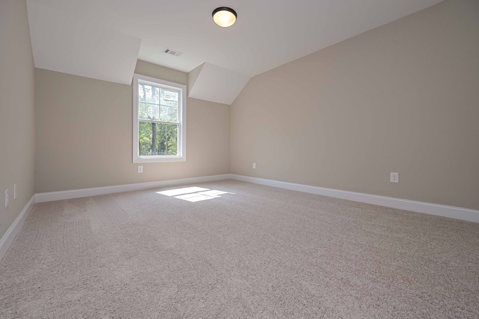 Empty beige bedroom with carpet, sloped ceiling, and a window letting in natural light
