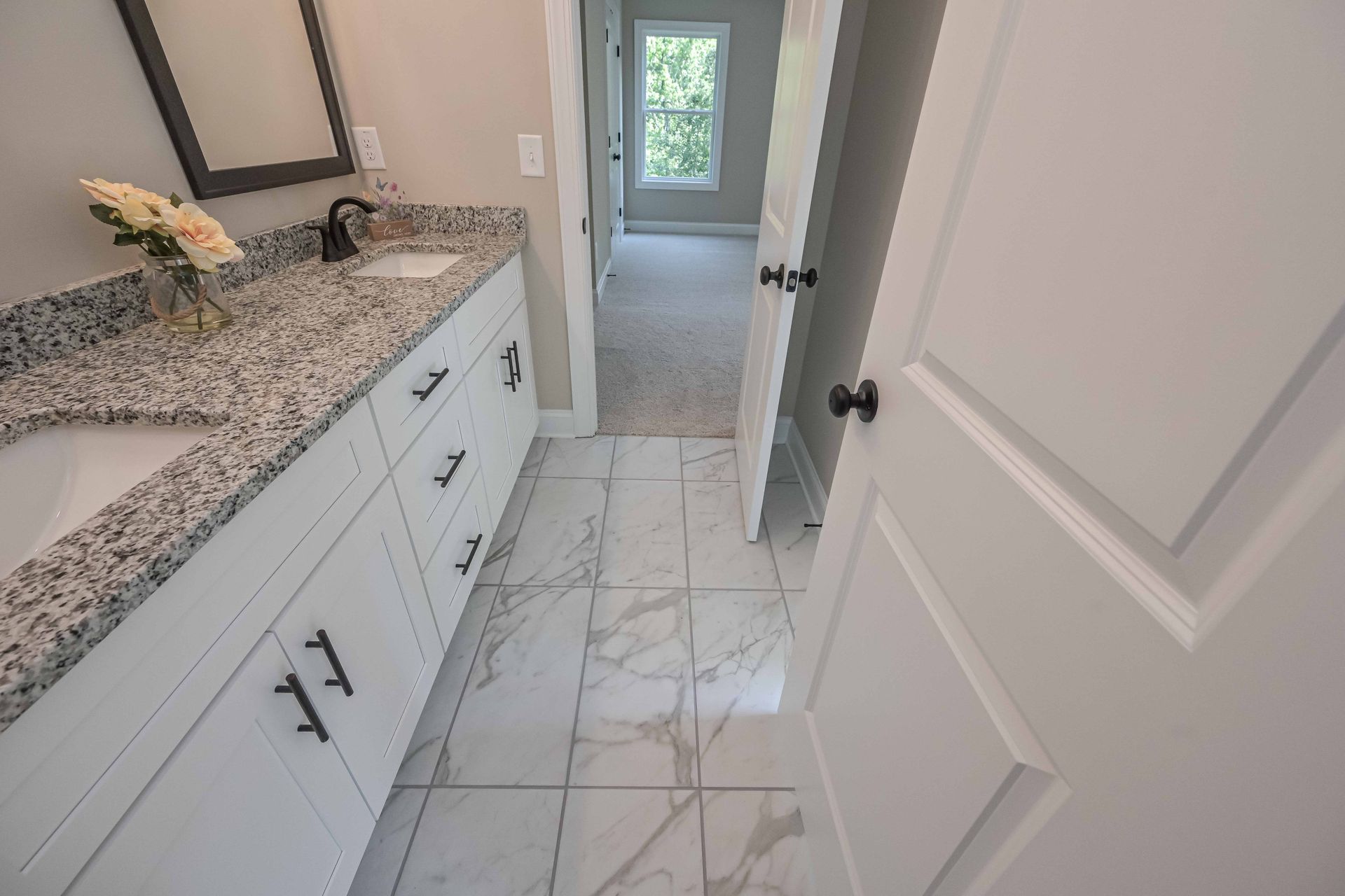 White bathroom vanity with granite countertop, marble floor, and open door to a small room beyond