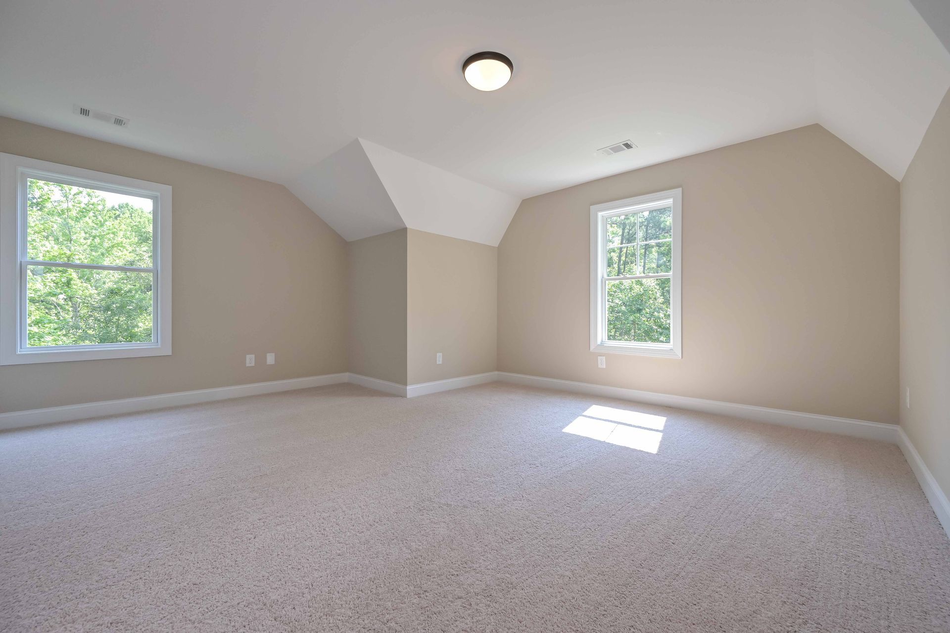 Empty beige bedroom with two windows and a carpeted floor￼