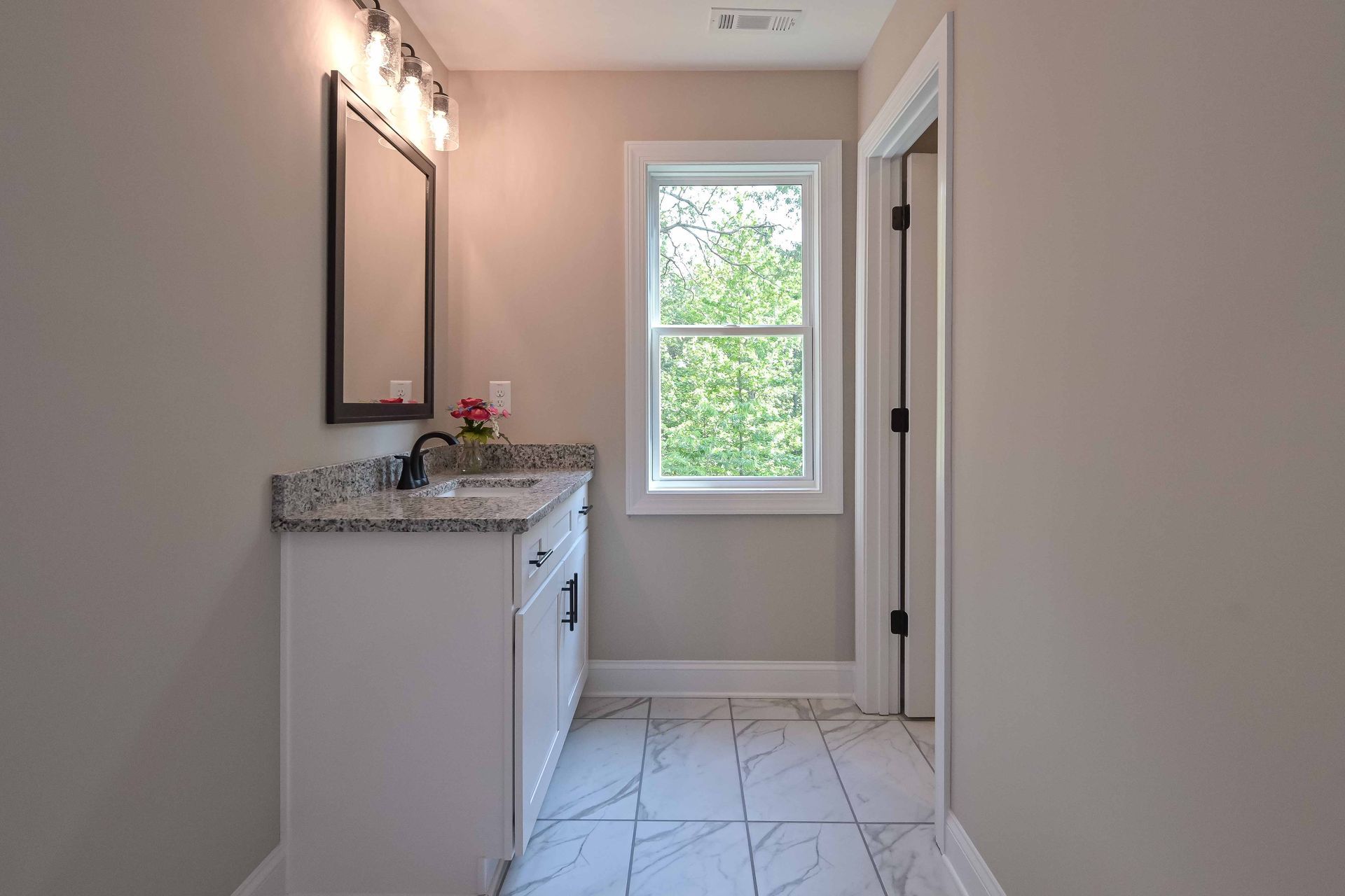 Narrow bathroom with white vanity, granite countertop, mirror, window, and light tile floor