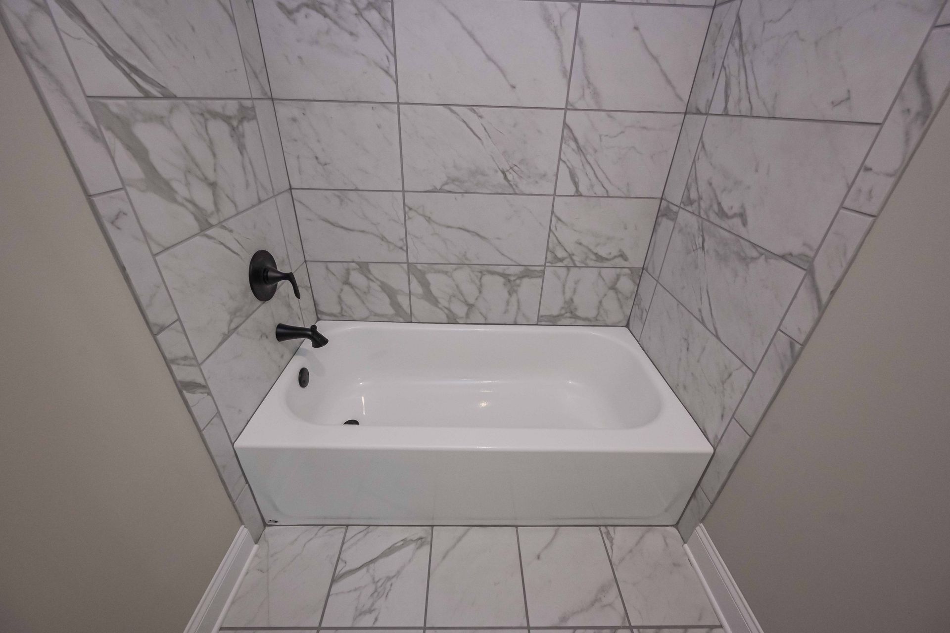 Small white bathtub with black faucet in a marble-tiled bathroom alcove.