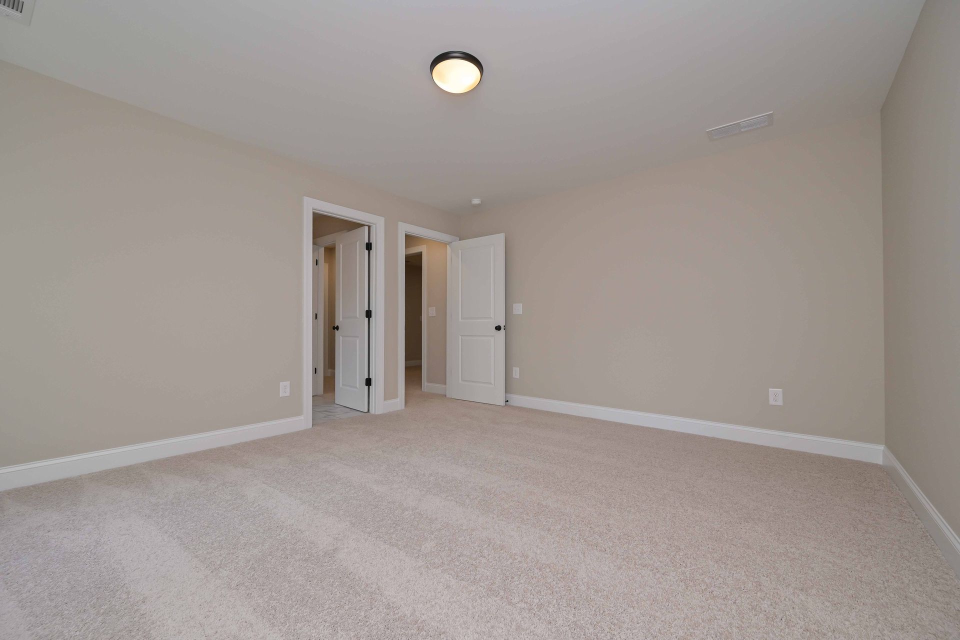 Empty beige carpeted bedroom with open closet and white door, lit by a ceiling light