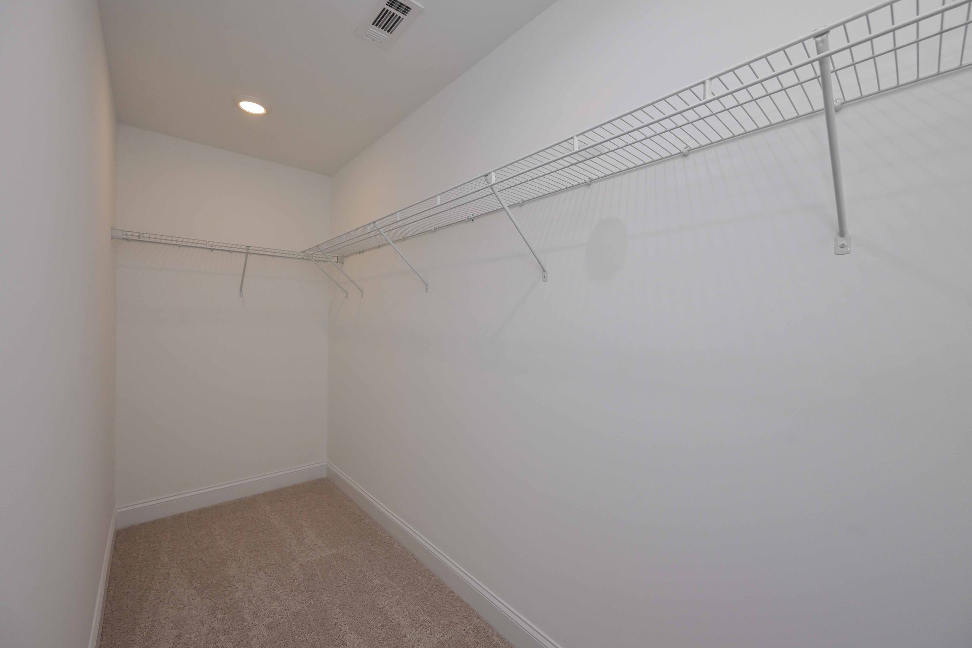 Empty walk-in closet with white wire shelving and beige carpeted floor.