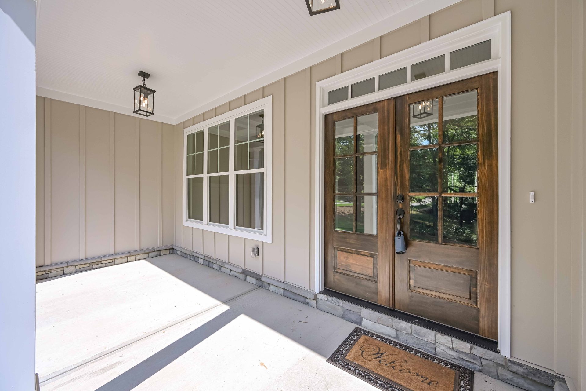 Covered front porch with beige siding, double glass front doors, and a window.