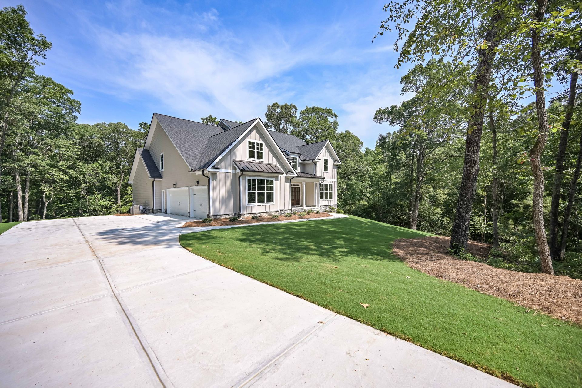 Suburban house with a long concrete driveway, green lawn, and trees under a blue sky