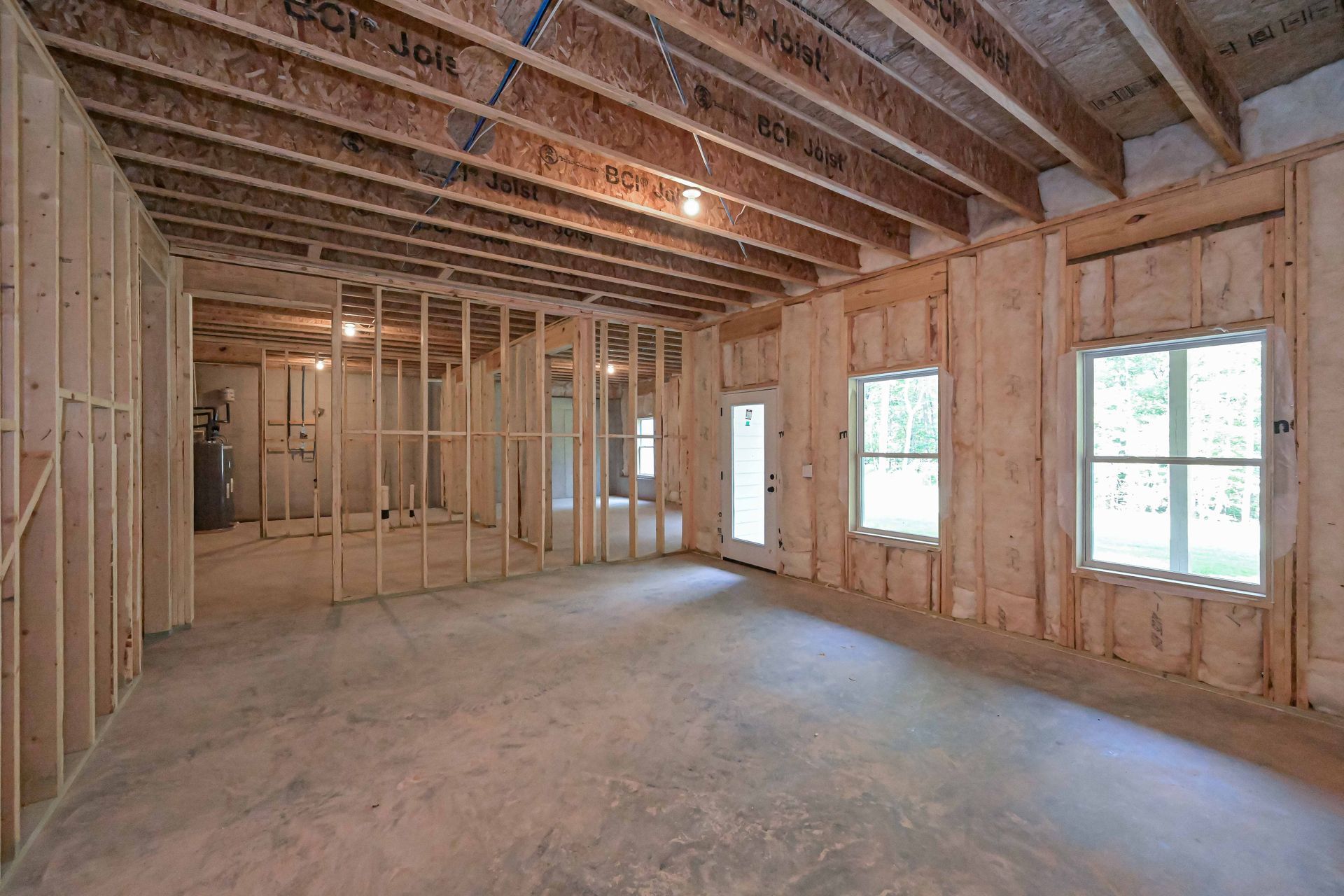 Unfinished framed room interior with exposed beams, wiring, and windows letting in daylight