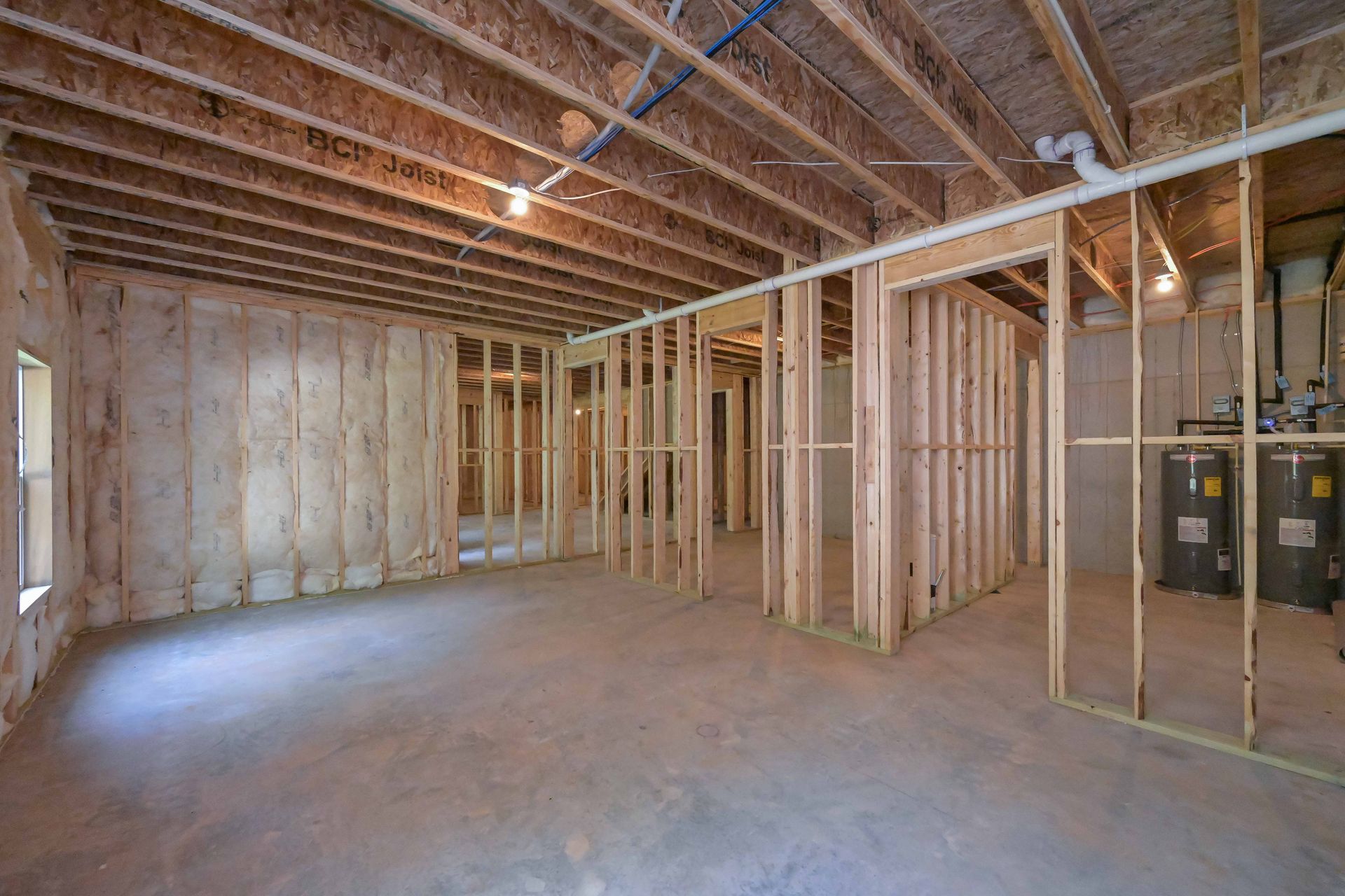 Unfinished basement with exposed wood framing, insulation, and concrete floor under bare ceiling joists