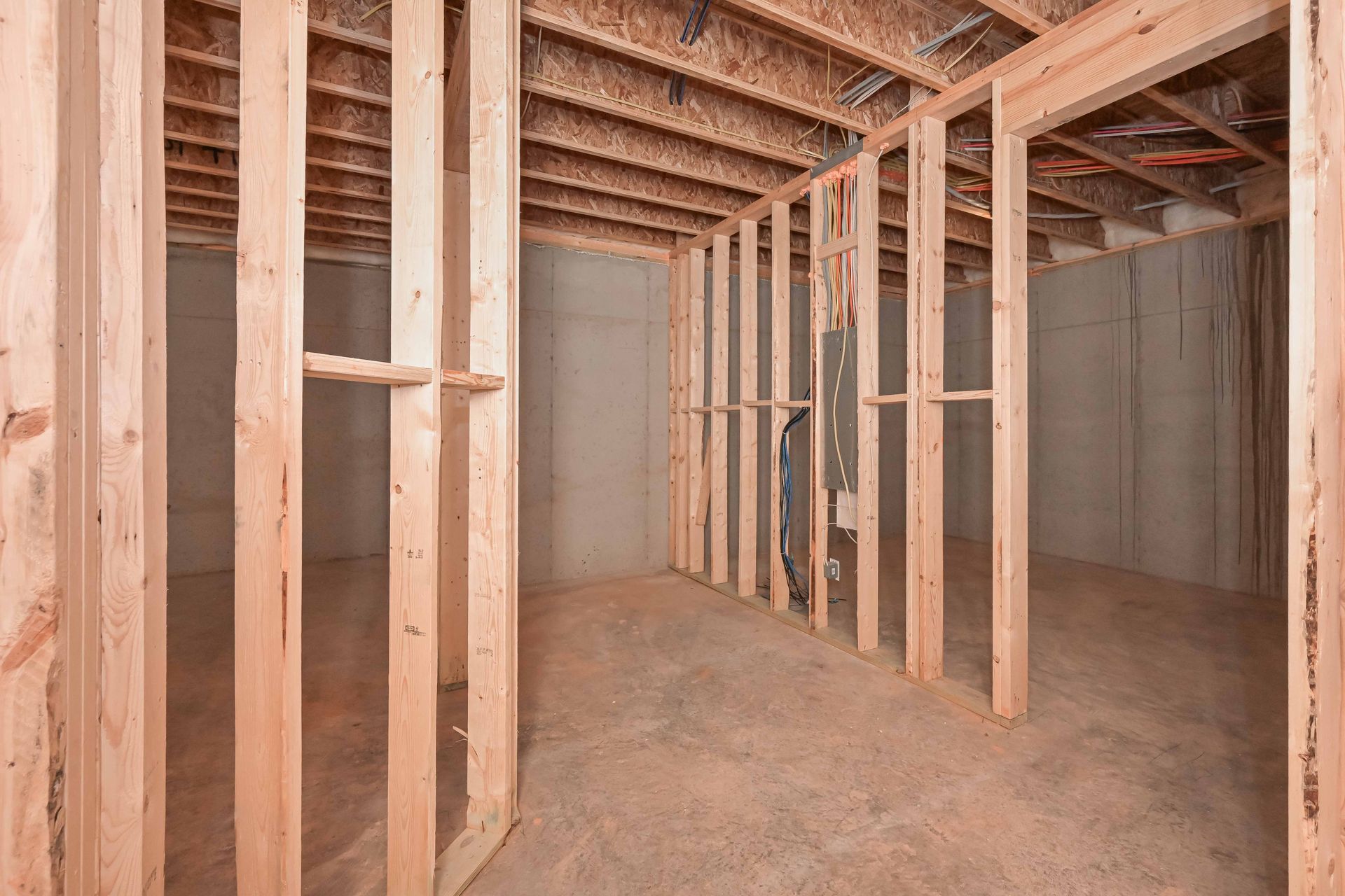 Unfinished basement framed with exposed wooden studs and joists, concrete floor, and walls under construction