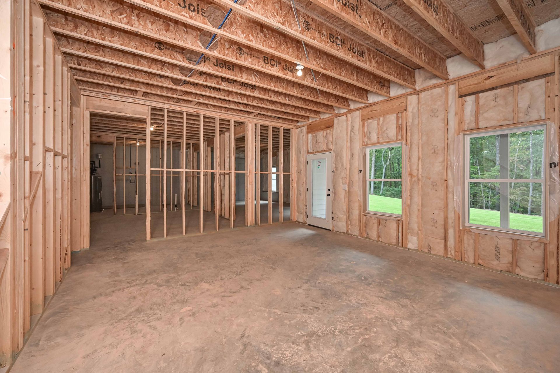 Unfinished house interior with exposed framing, dirt floor, and windows letting in daylight