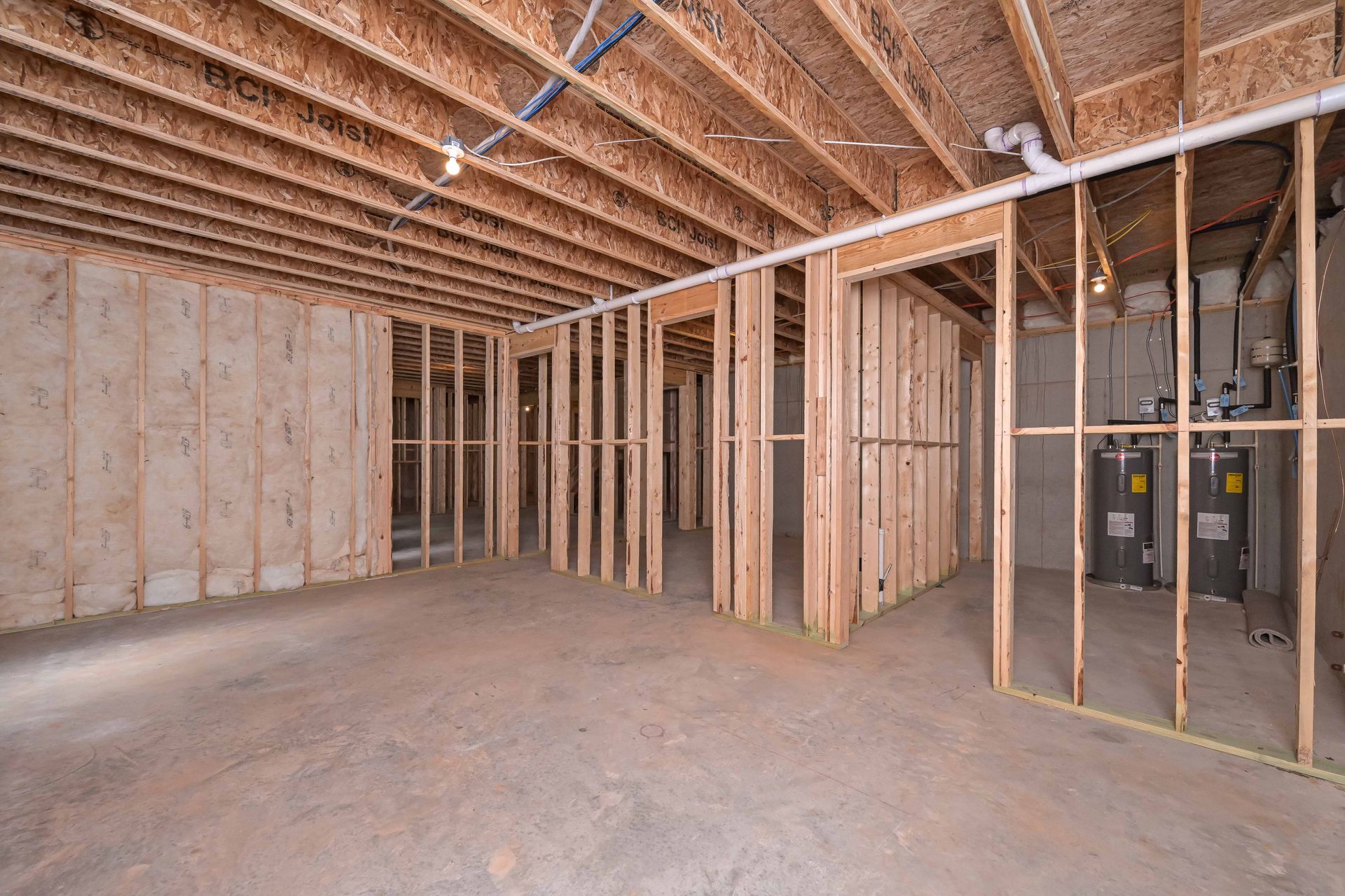 Unfinished attic with exposed wooden framing, insulation, and concrete floor.